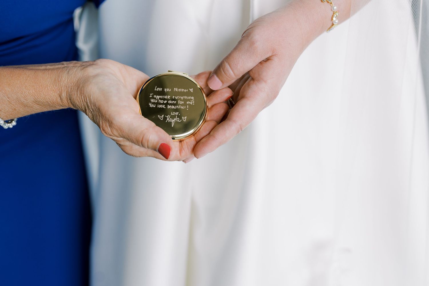 Two hands hold a small round gold engraved compass against a white and blue background.