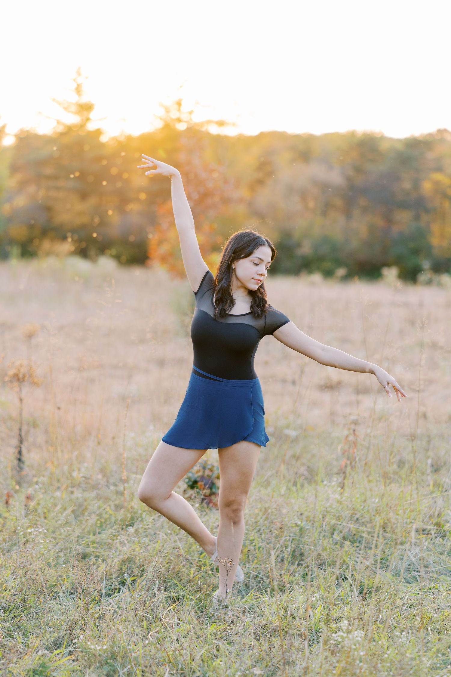 Dancer performs graceful movements in a sunlit meadow at golden hour wearing a black top and blue shorts.