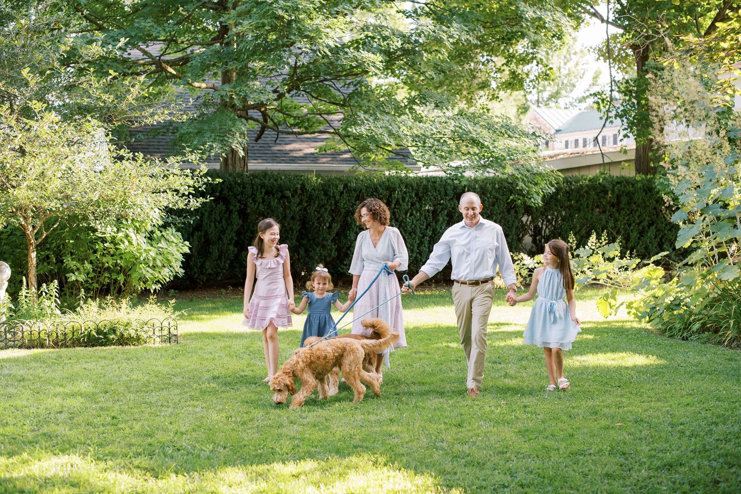 Family members walking with their dogs across a sunlit lawn during a photo session.