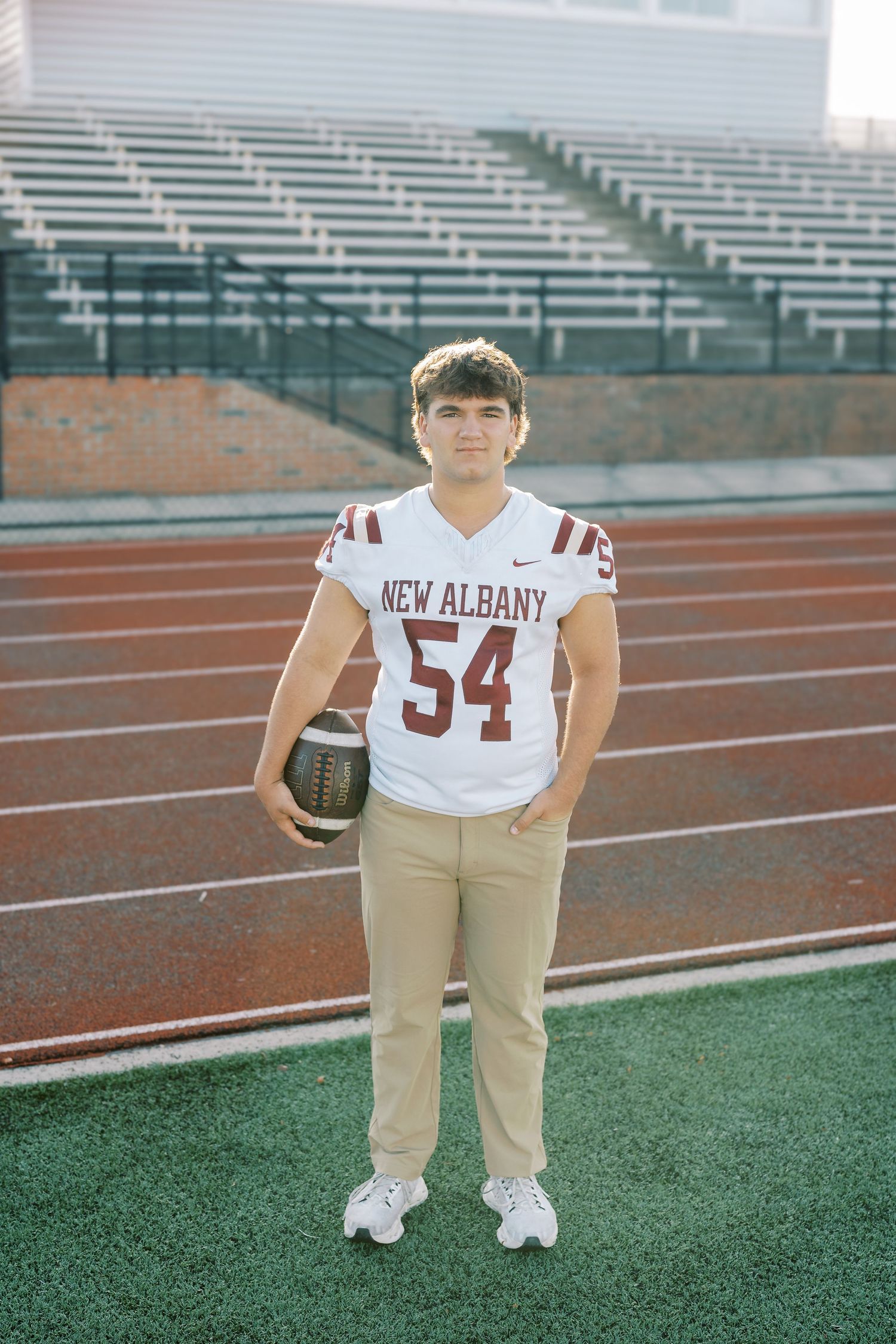 Football player in white and khaki uniform poses on field at stadium bleachers in panoramic series of shots.