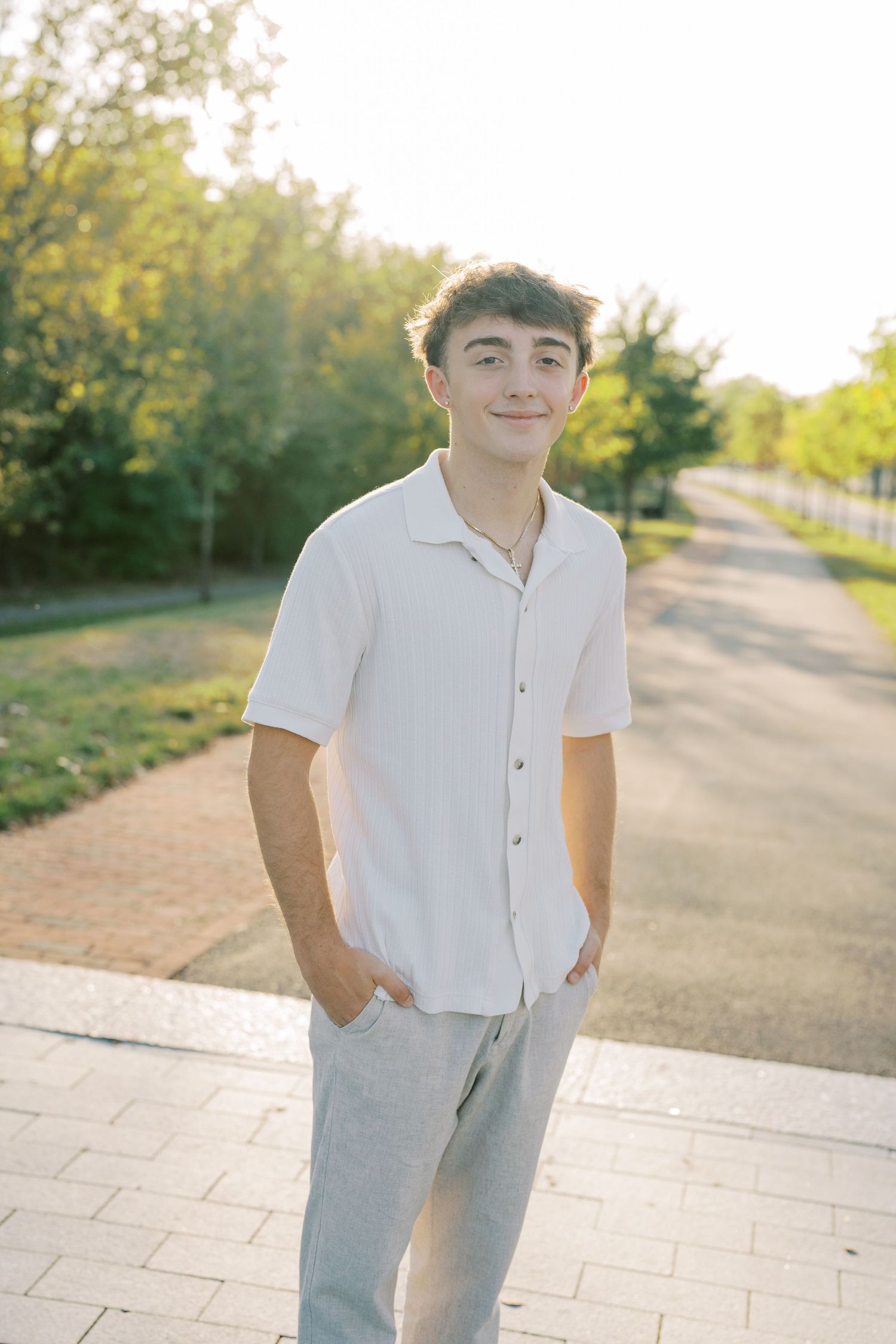 A person in a white button-down shirt and light pants stands on a sunlit path during golden hour.