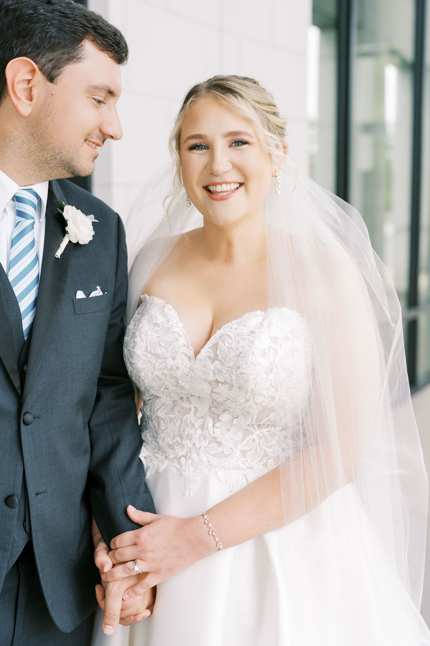 A bride and groom share joyful moments together in a bright indoor setting with modern glass windows.