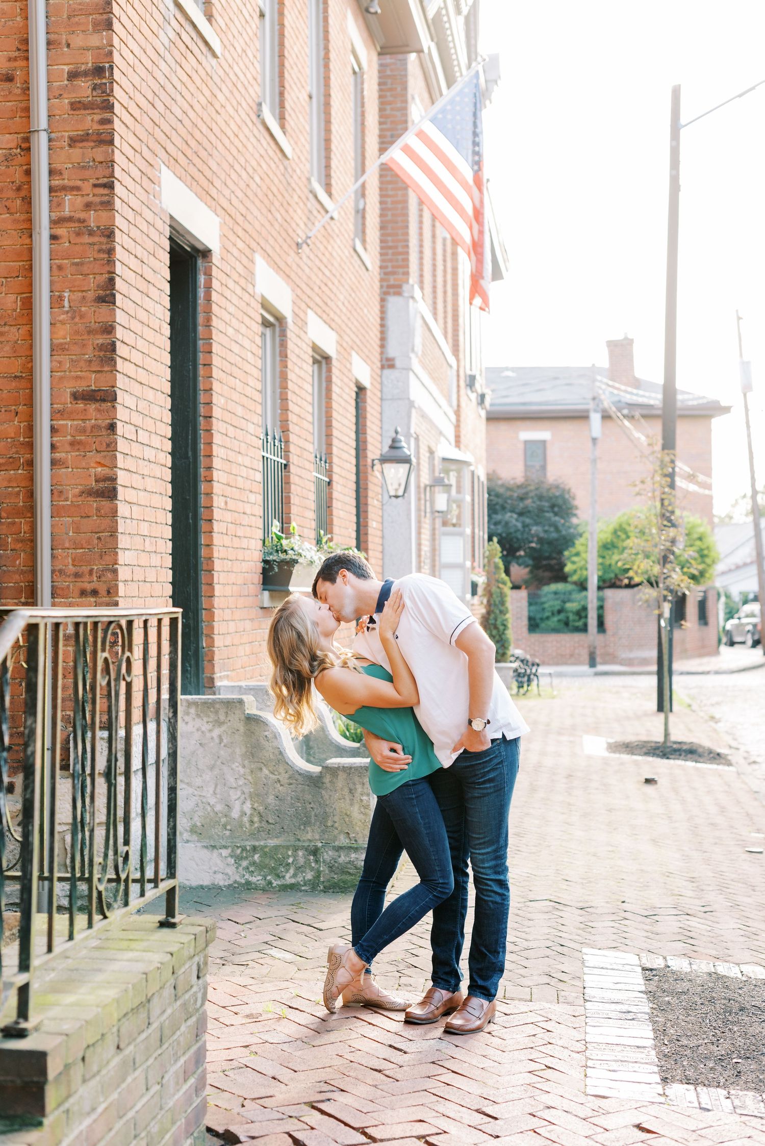 A couple shares romantic moments on a brick-lined street with classic architecture and lamp posts in the background.