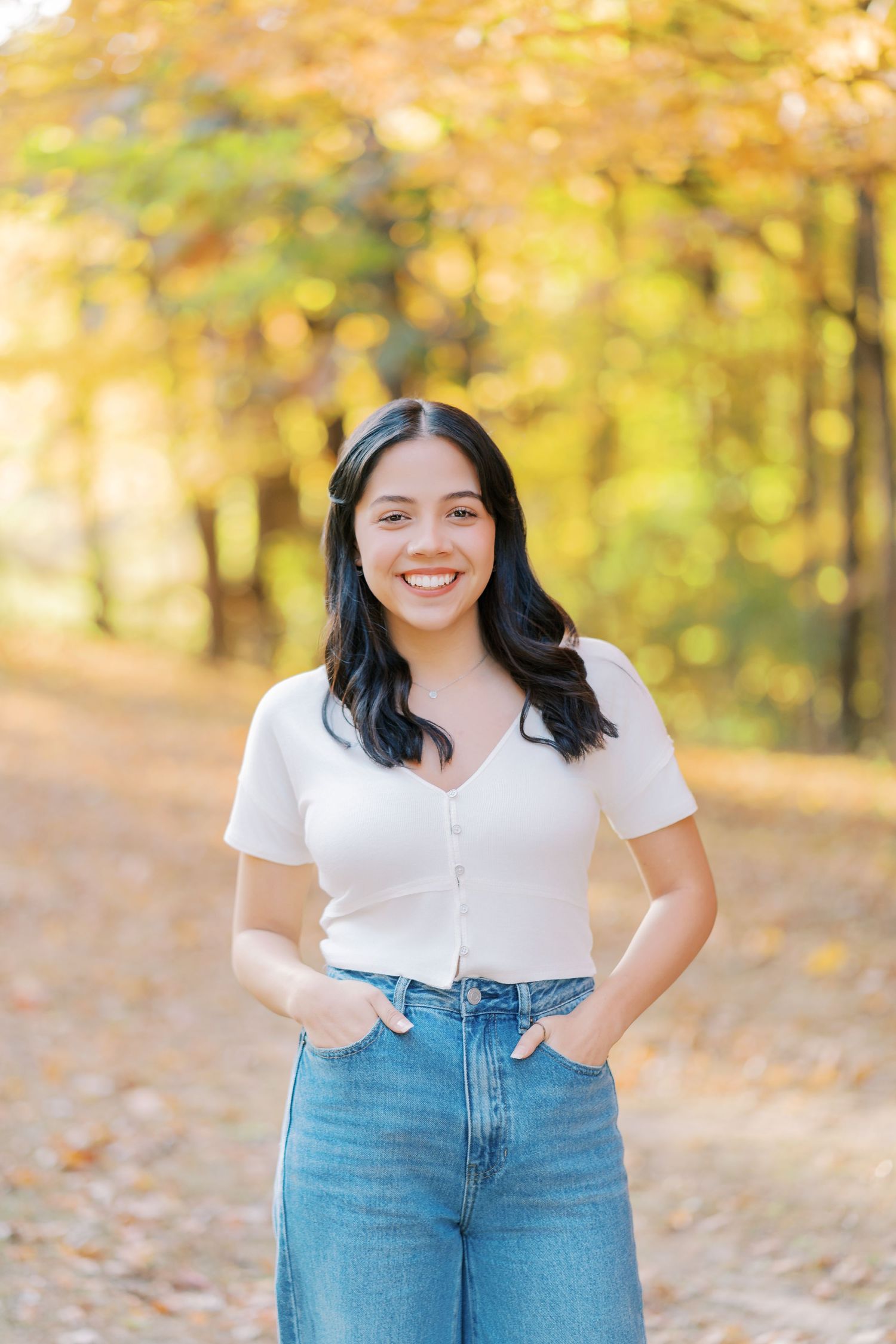 Casual autumn outdoor portrait showing someone wearing a white t-shirt and blue jeans against a golden fall background.