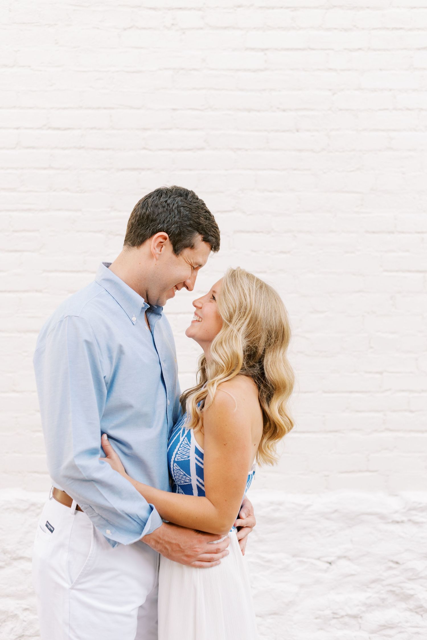 A romantic couple embraces on a bright white beach wearing coordinated blue and white outfits.