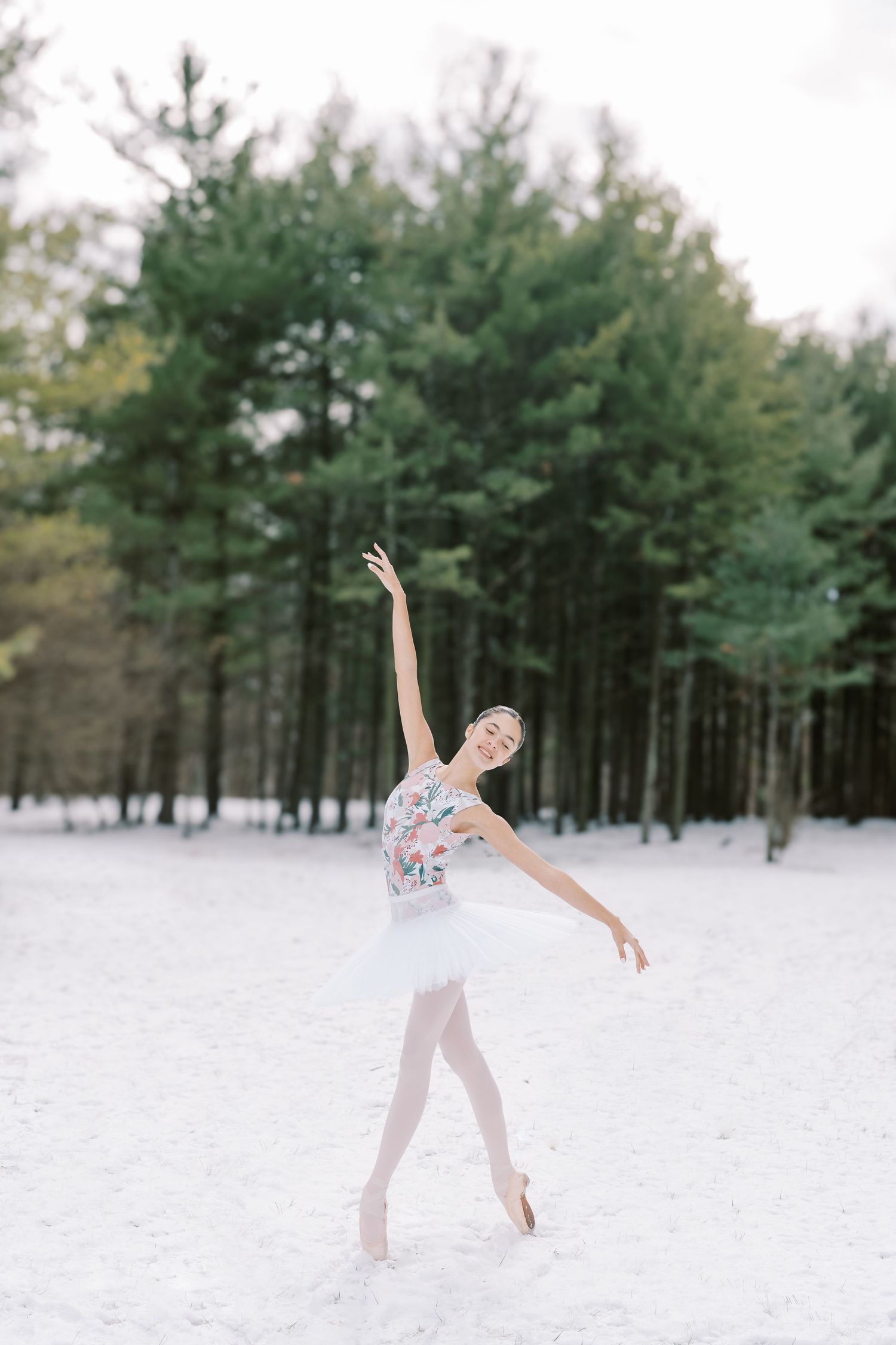 A dancer in a flowy white dress performs graceful movements in a snowy forest landscape.