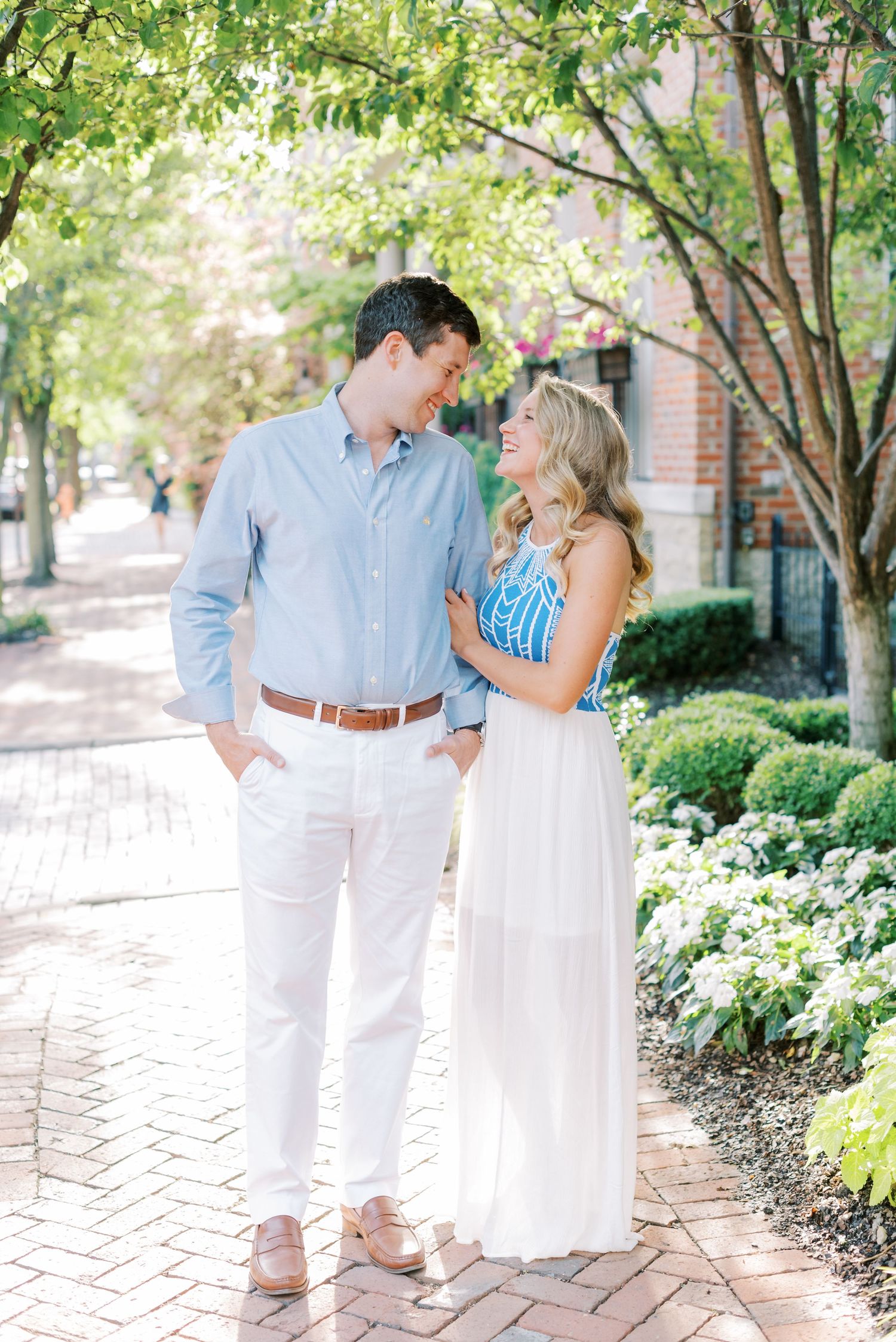 Couple in coordinated blue and white outfits share romantic moments along a brick pathway surrounded by greenery.