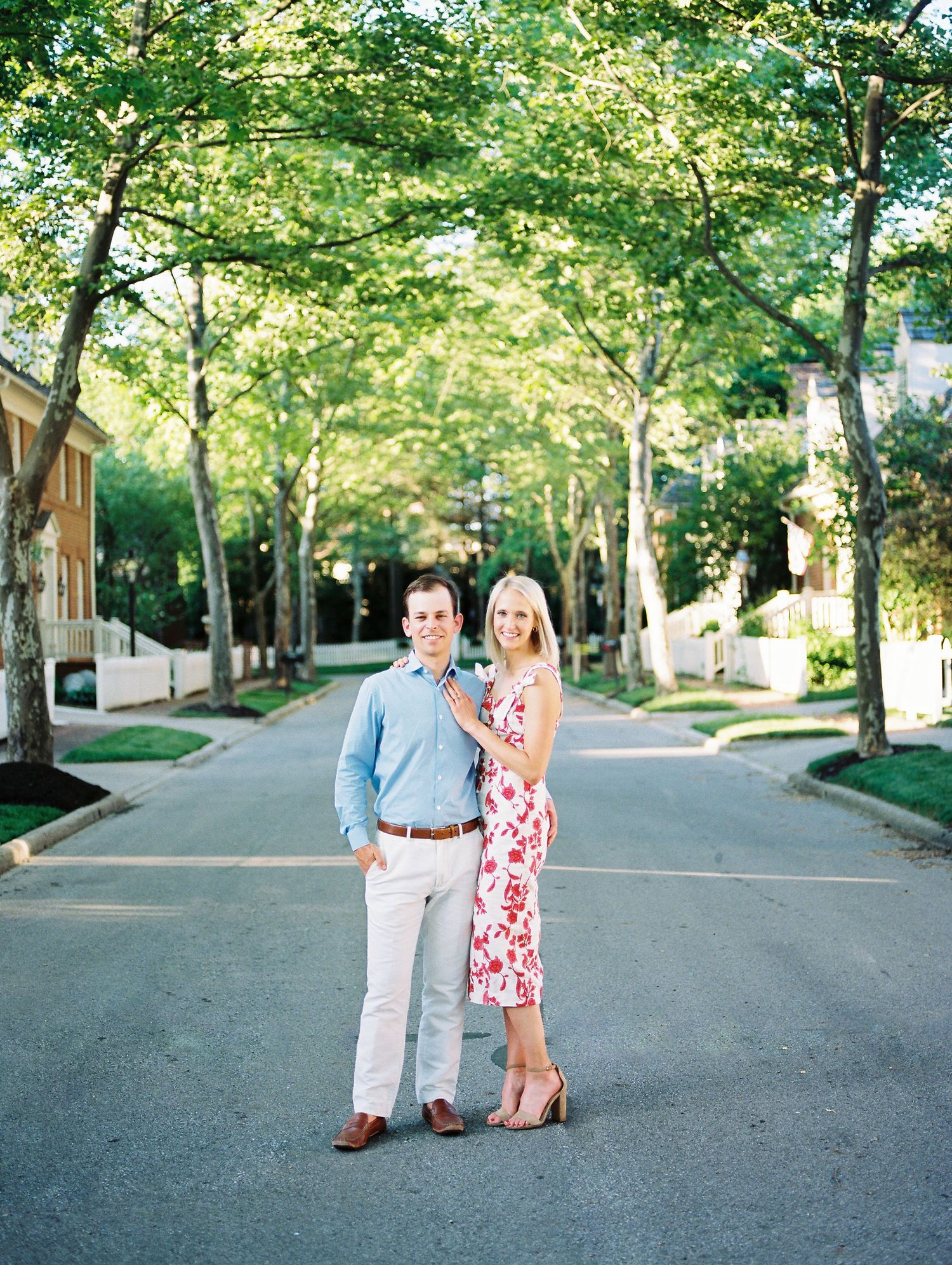 A couple enjoys a romantic stroll down a tree-lined street on a sunny summer afternoon.