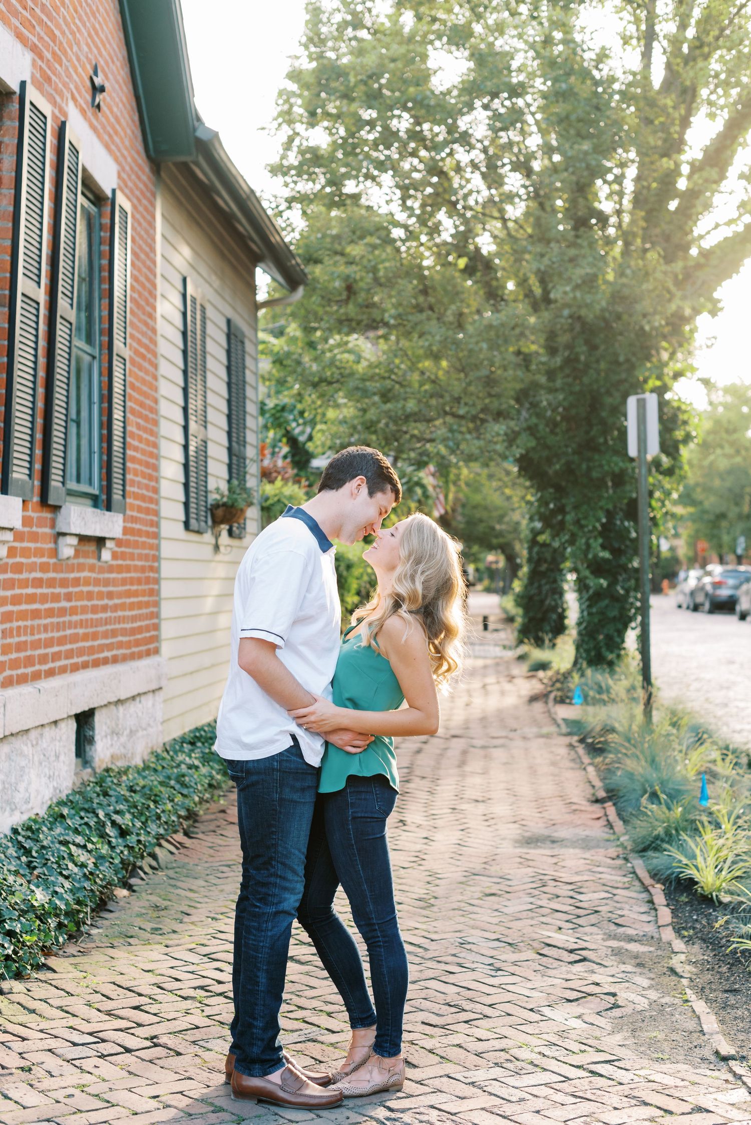 A romantic couple shares tender moments on a brick walkway surrounded by greenery and ivy during a photo session.