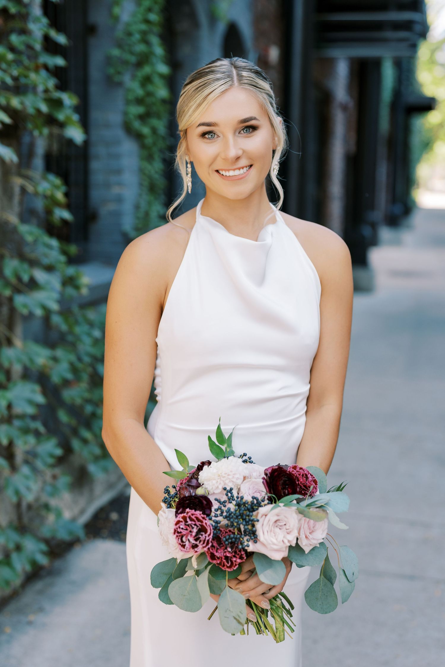 A person in a sleeveless white dress holds a romantic bouquet of burgundy and blush flowers with eucalyptus.