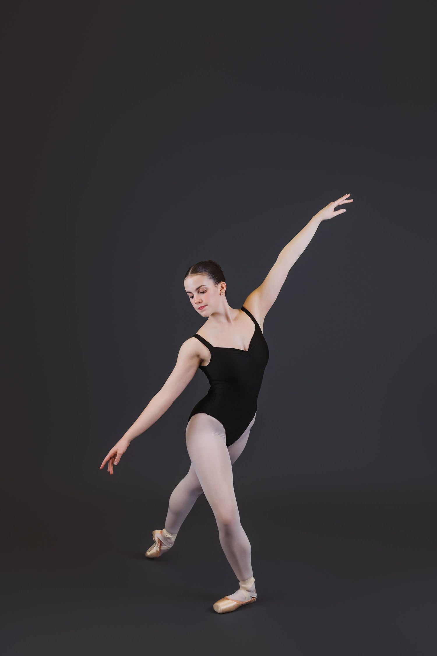 Ballet dancer in black leotard and pink tights performs graceful dance poses against dark background.