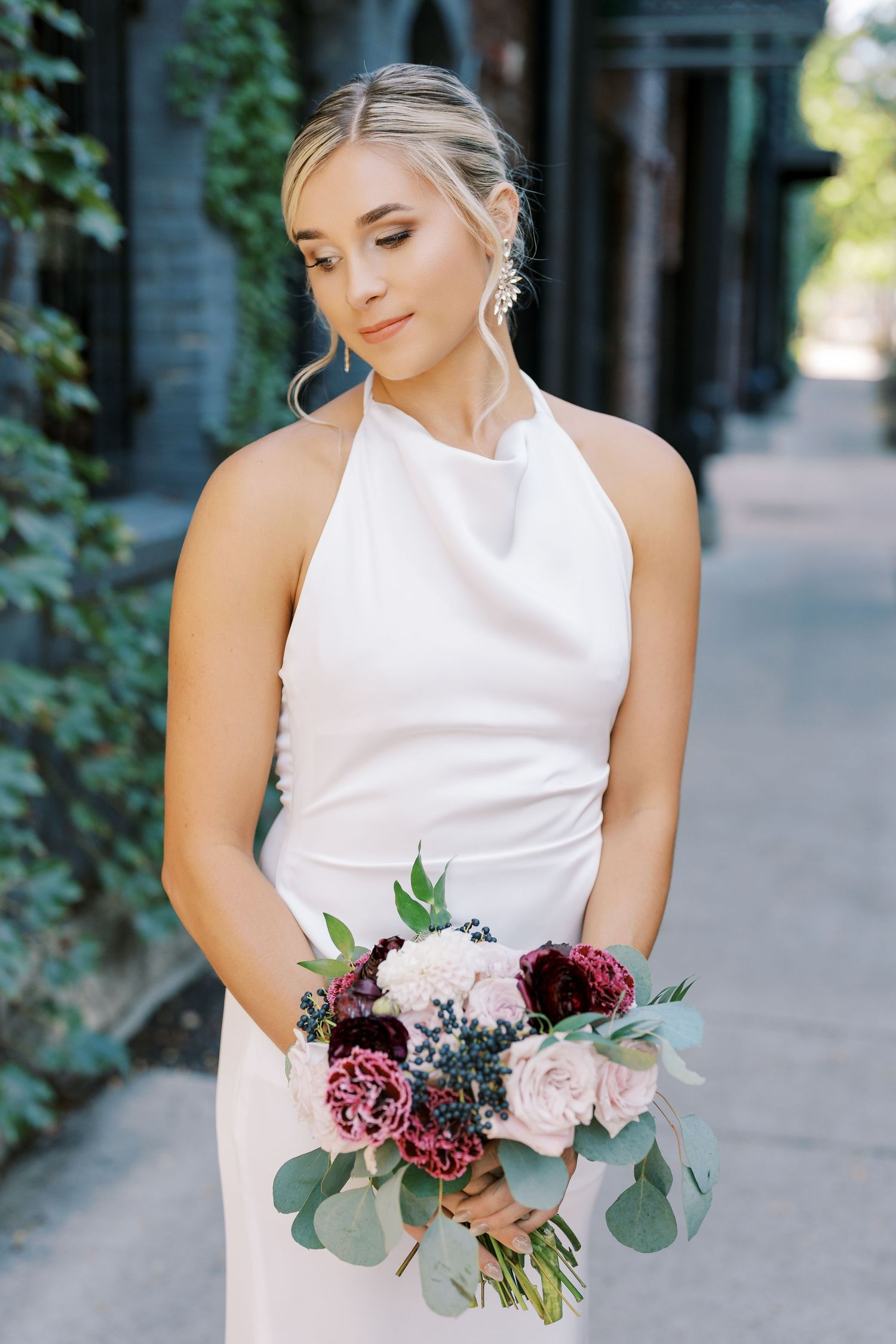 A bride in a sleeveless white dress holds a romantic bouquet of burgundy and blush flowers with eucalyptus.