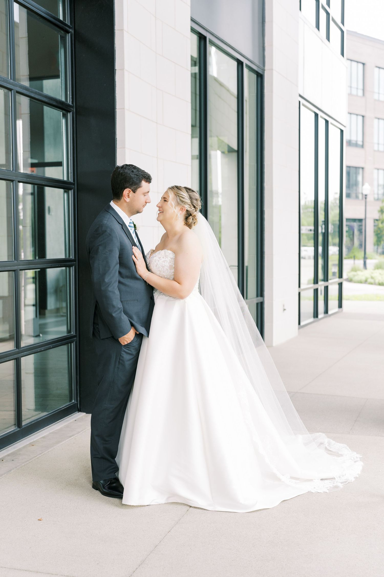 A bride and groom share an intimate moment in a modern hallway with floor-to-ceiling windows.