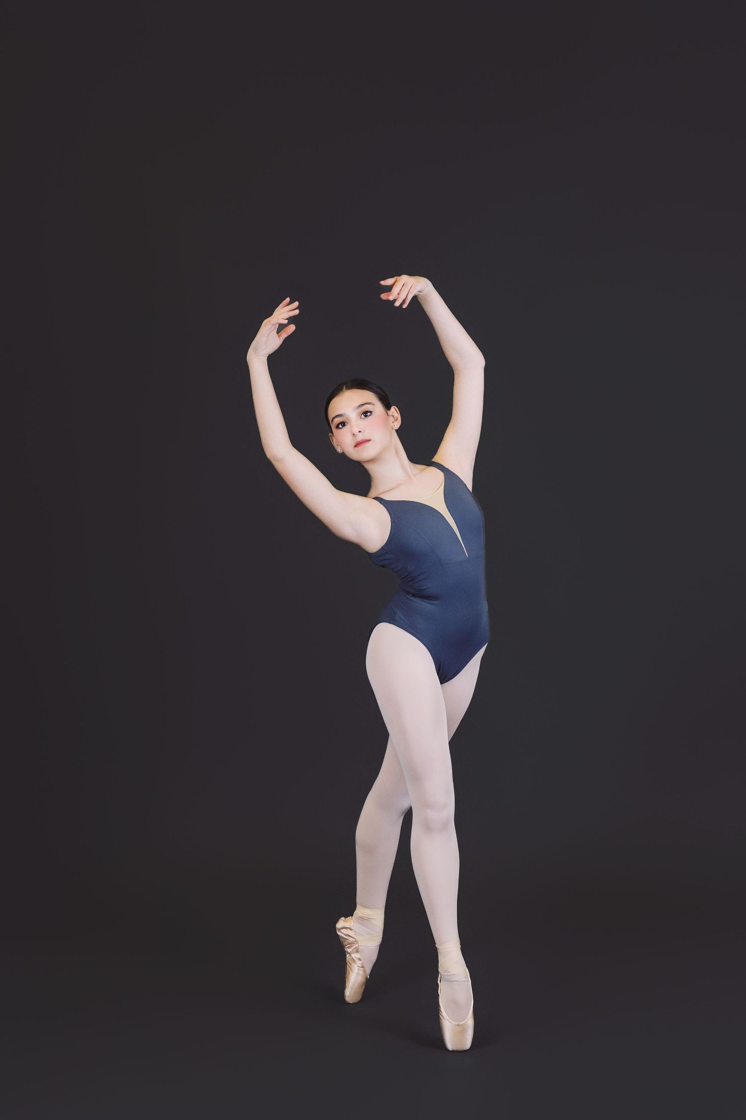 Ballet dancer in navy leotard and white tights performs graceful poses in sequence against dark background.