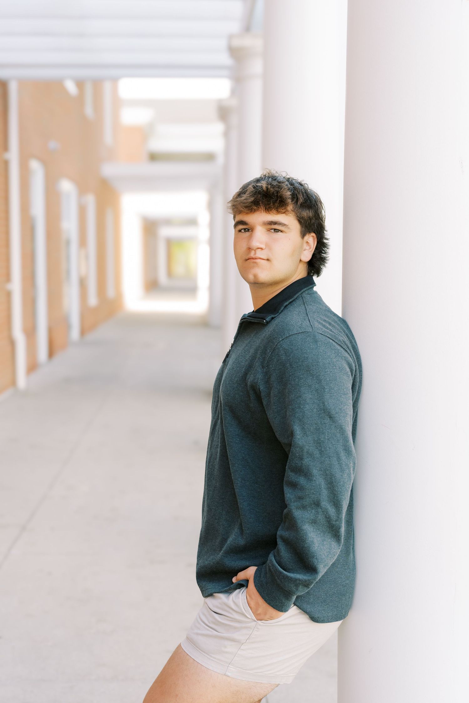 Three artistic portraits of a person wearing a navy sweater and white shirt against a bright minimalist hallway background.