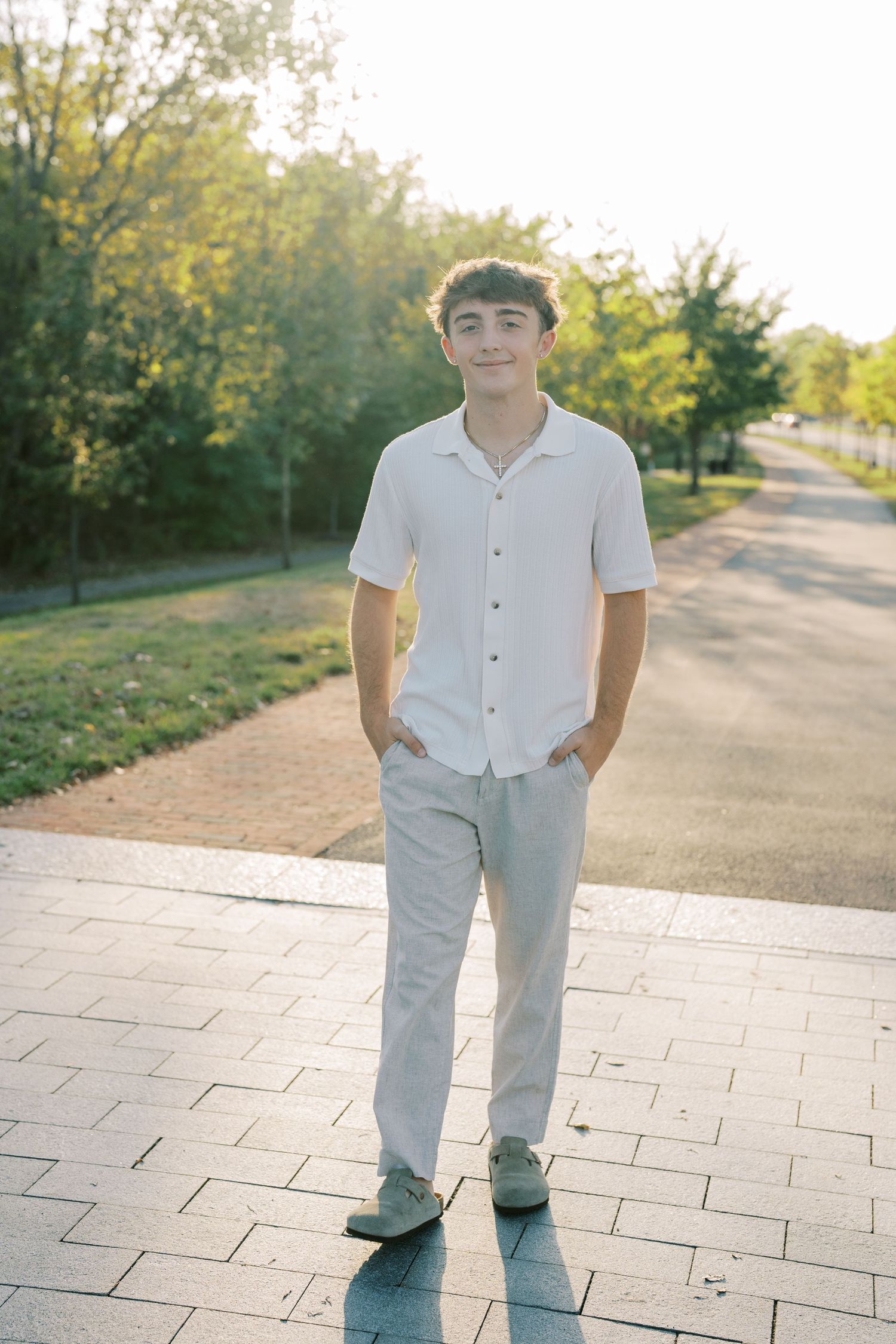 Someone wearing light colored clothing stands on a paved pathway in a park during golden hour.