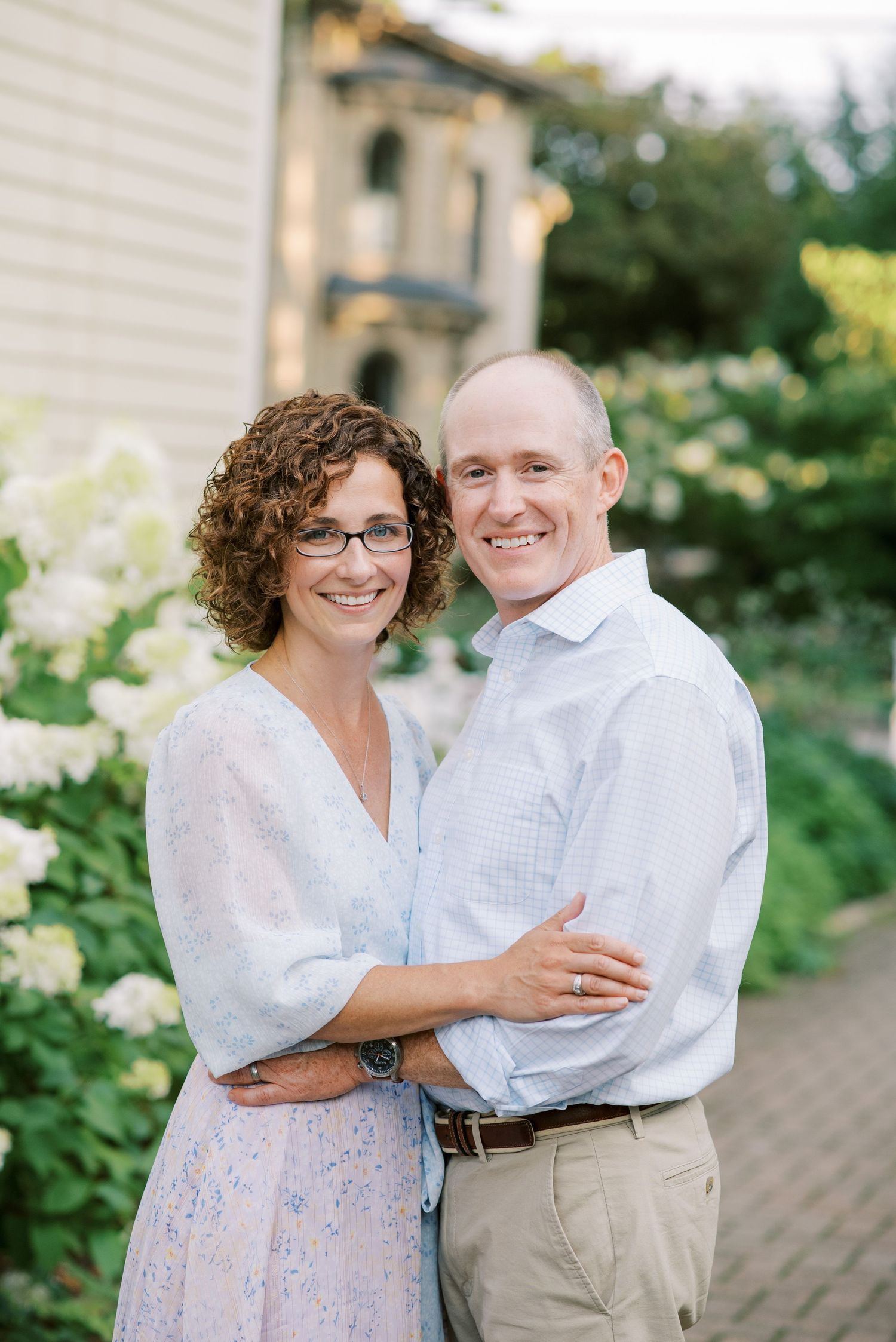 Couple in casual attire embracing on garden path with white hydrangeas.