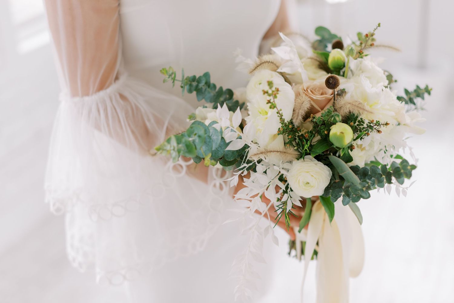 Elegant white bridal bouquet with roses and greenery against a light background.
