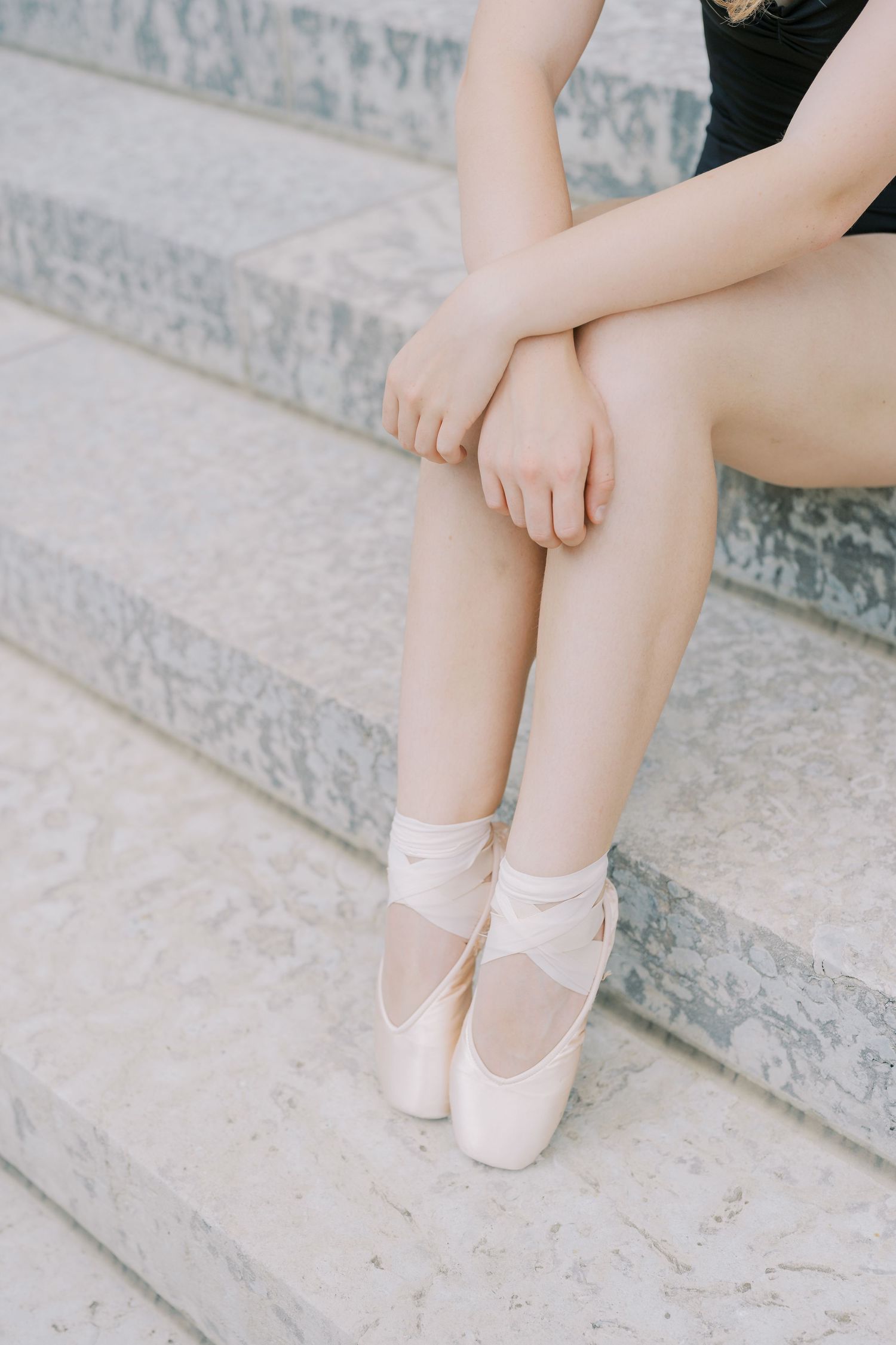 Ballet dancer's feet in pink satin pointe shoes resting on concrete steps in soft natural light.