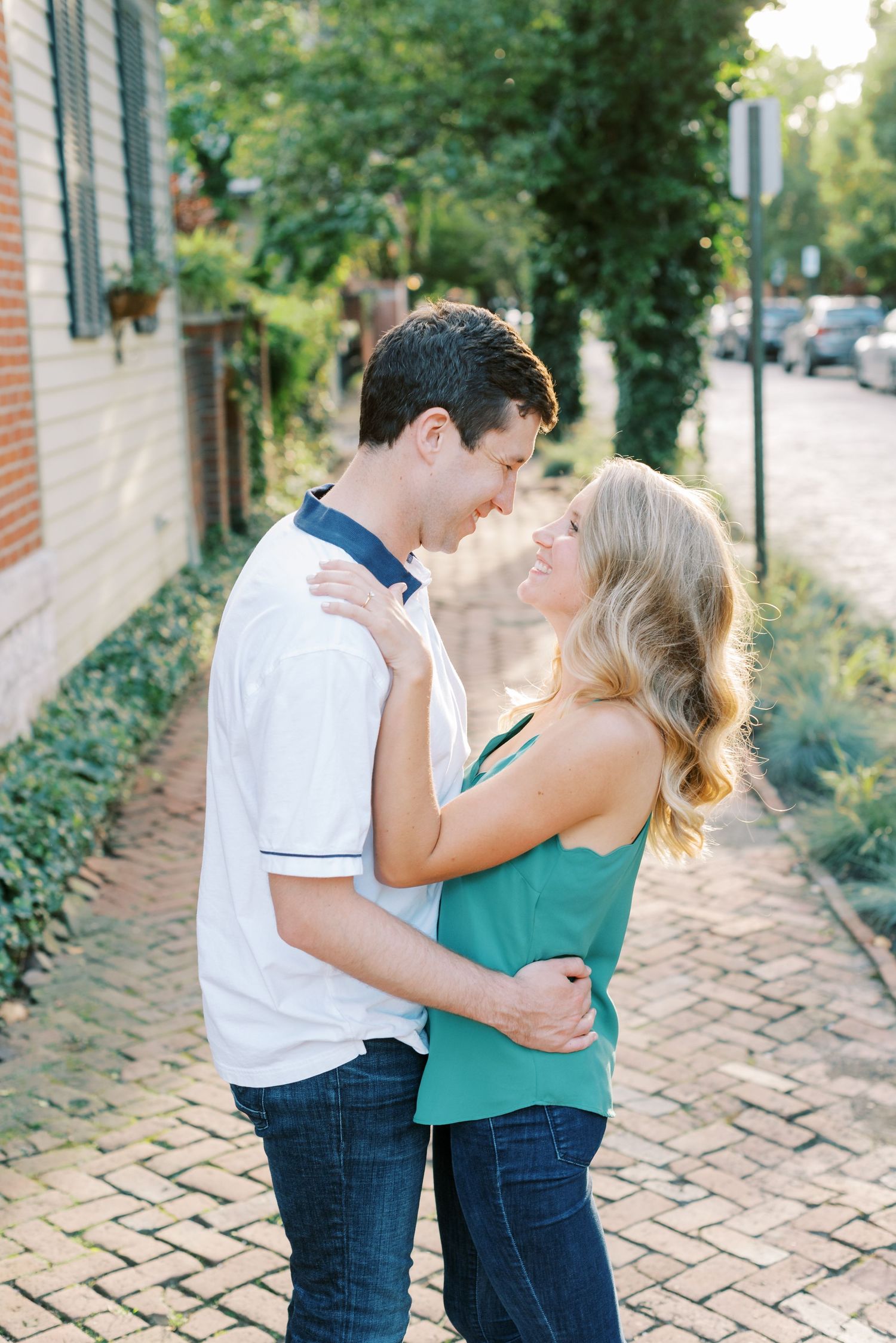 A couple embraces on a charming brick sidewalk lined with greenery on a sunny afternoon.