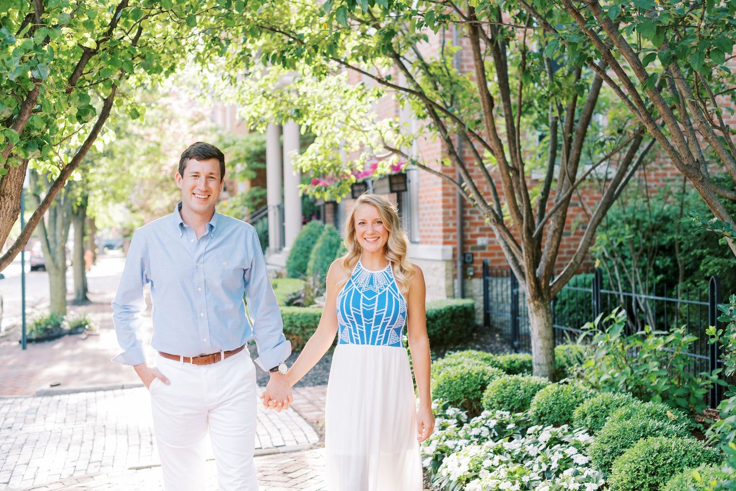A couple poses together in a garden setting wearing coordinated blue and white summer outfits.