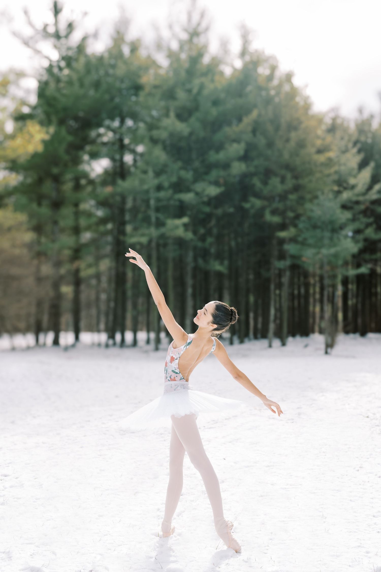 A dancer performs a graceful sequence of movements in the snow with evergreen trees in the background.