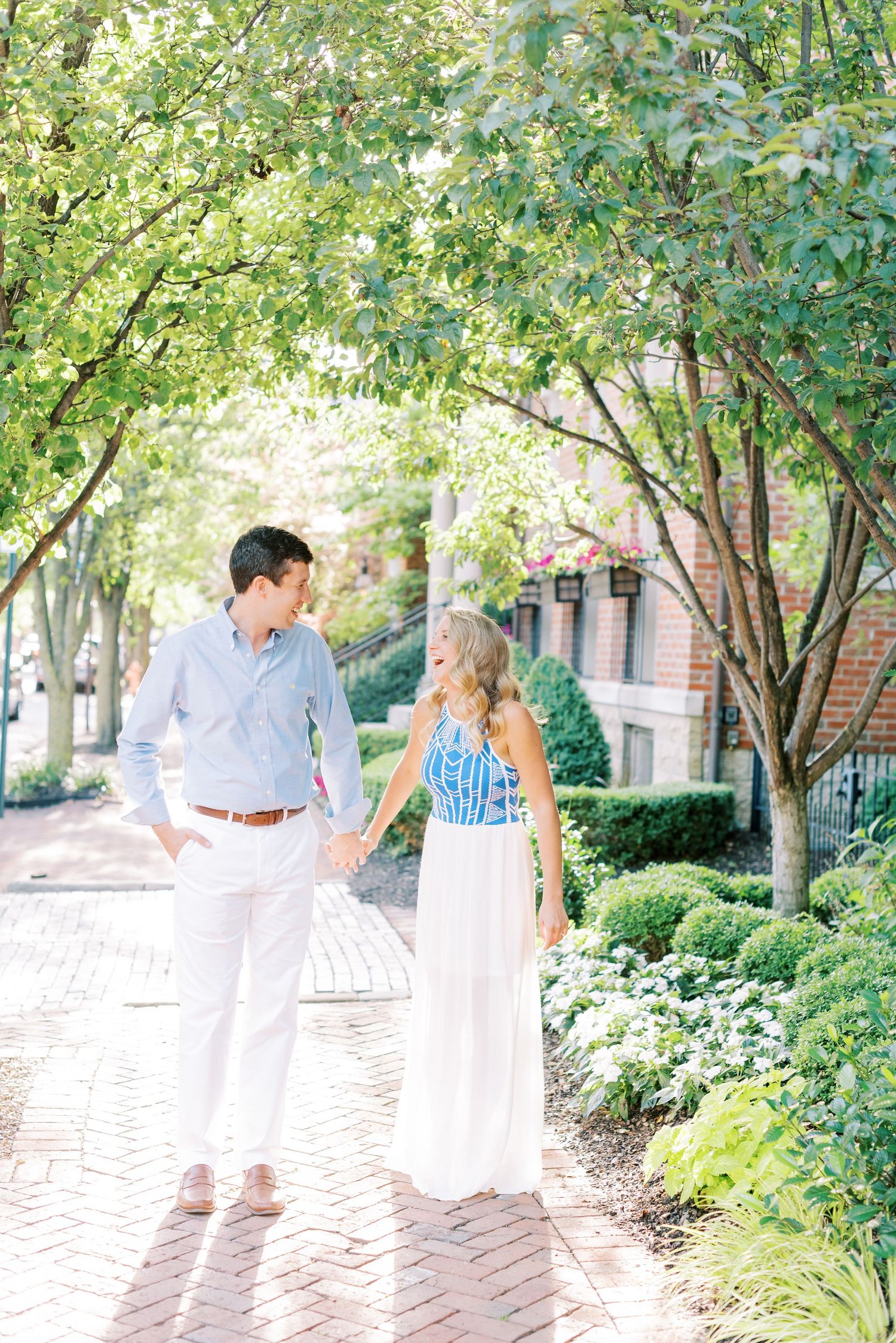 A couple shares romantic moments along a brick pathway surrounded by lush greenery on a sunny afternoon.