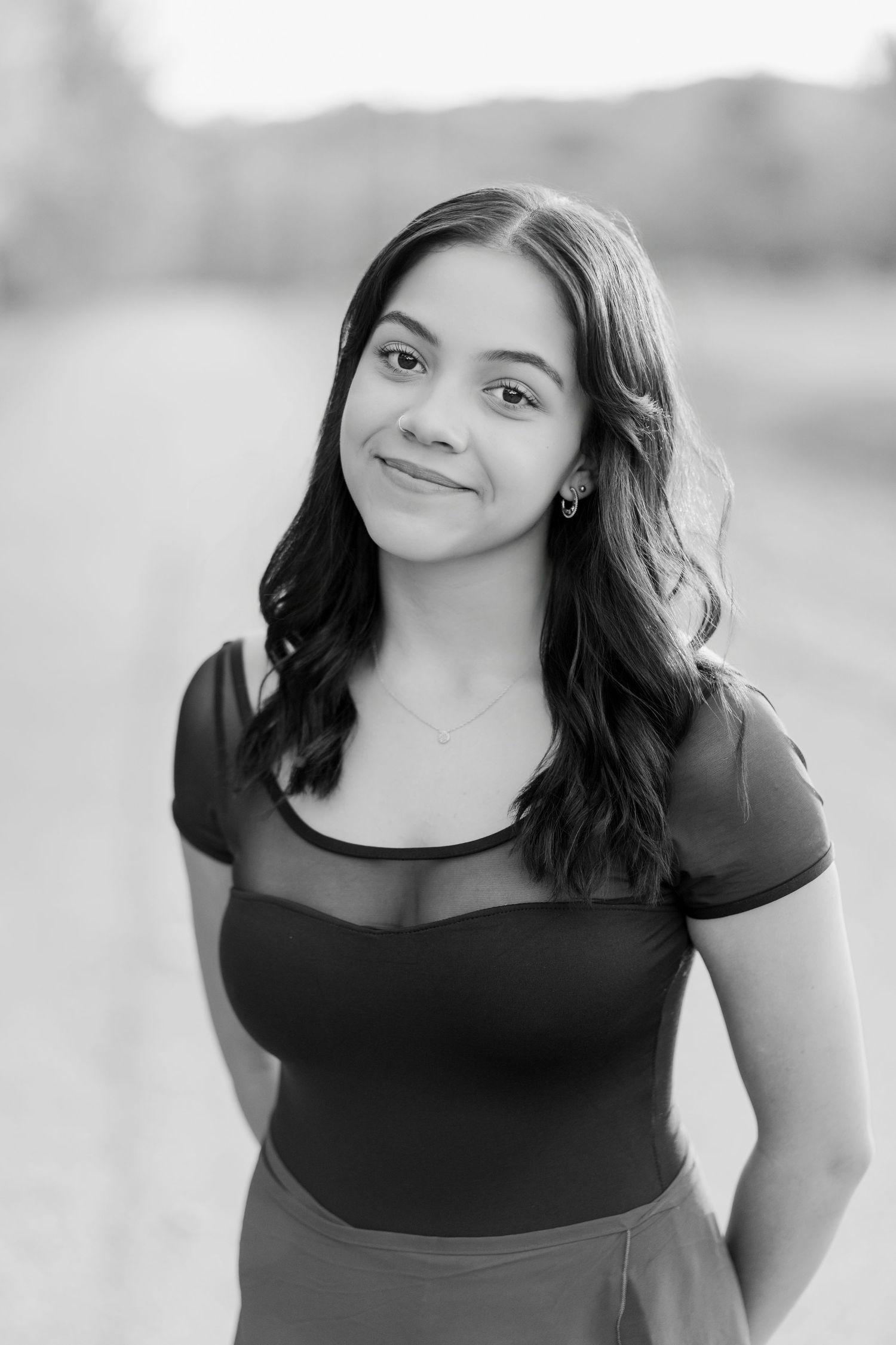 Black and white portrait of a young woman in a dark top smiling at the camera outdoors.