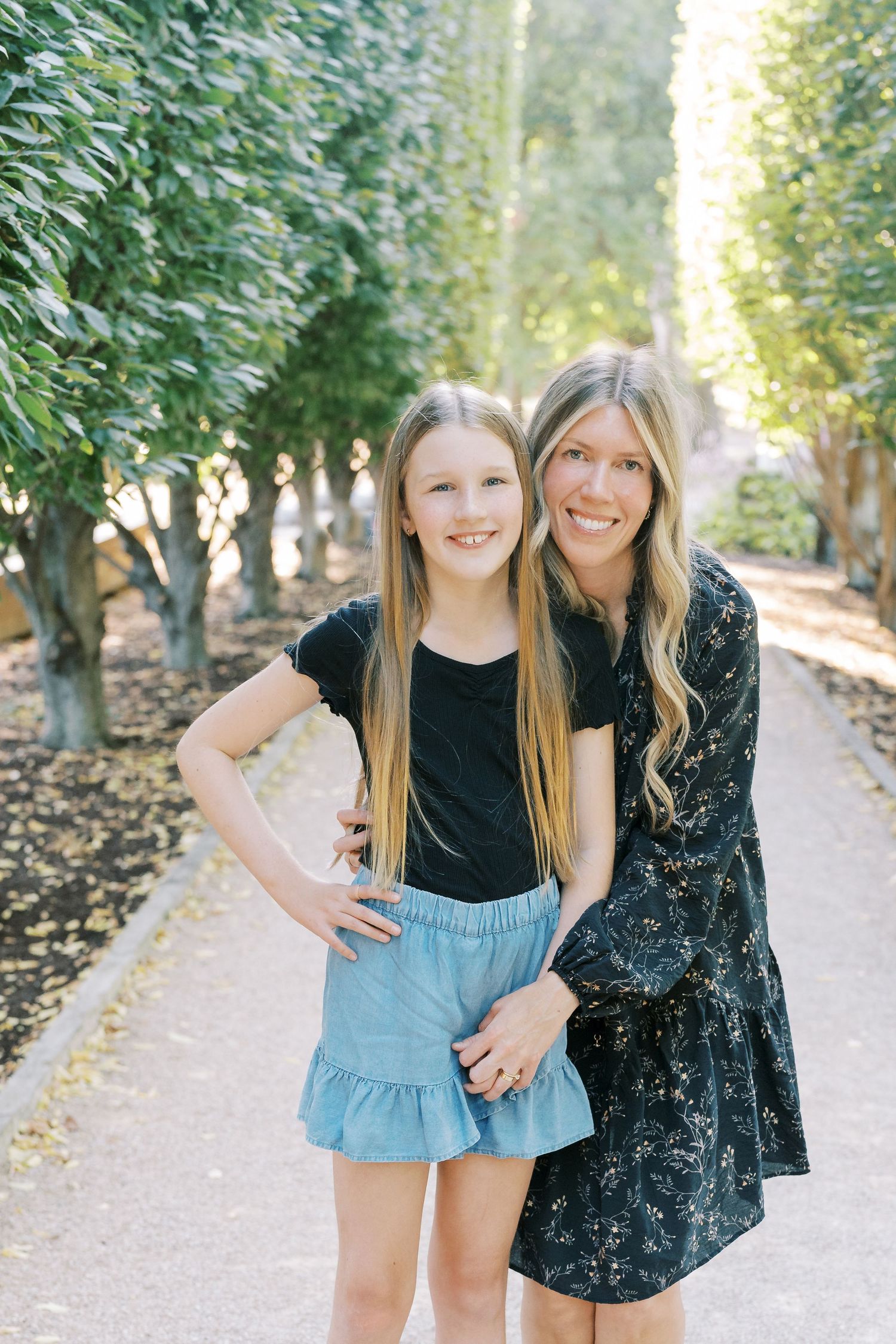 Mother and daughter portrait session on tree-lined garden path.
