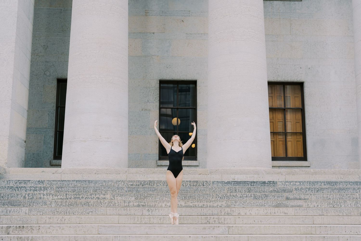 Dancer silhouetted against white architectural columns in artistic pose.