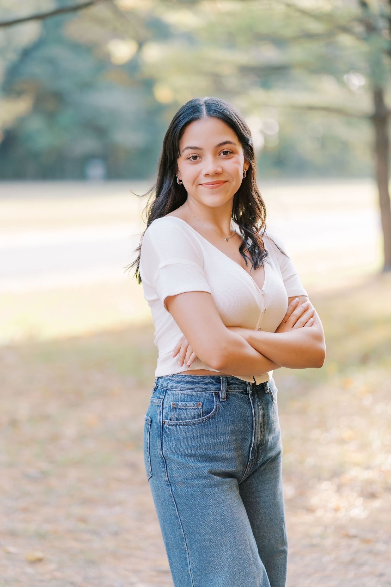 A person in jeans and white top poses casually outdoors in natural sunlit setting.