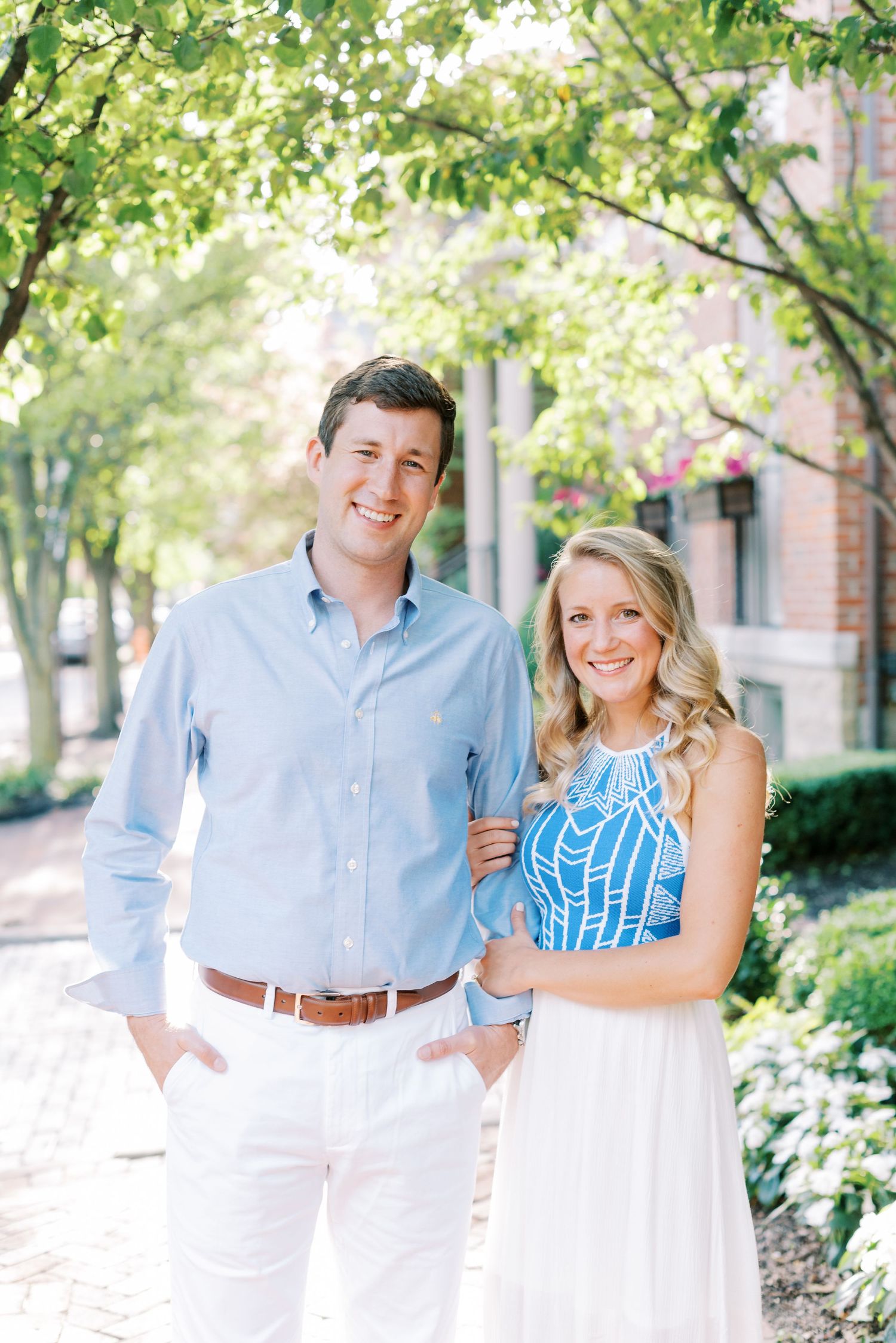A couple in coordinating blue and white outfits pose together for engagement photos in a garden setting.