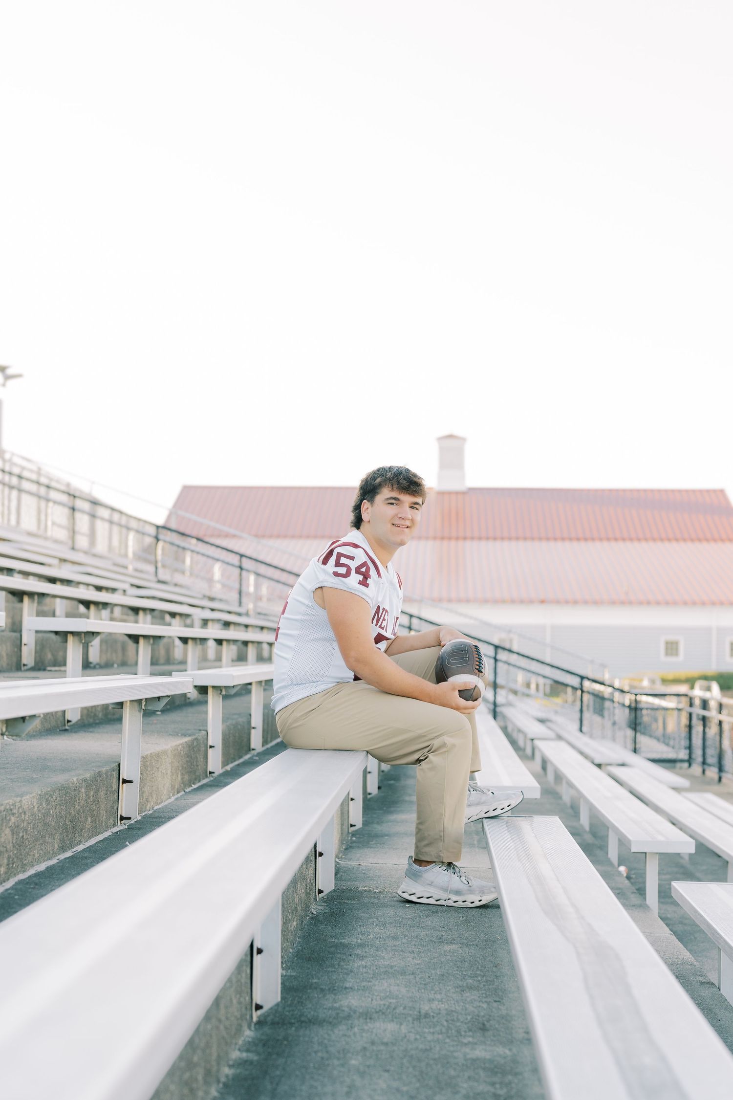 Person in a white jersey sits alone on concrete stadium bleachers in a contemplative pose.