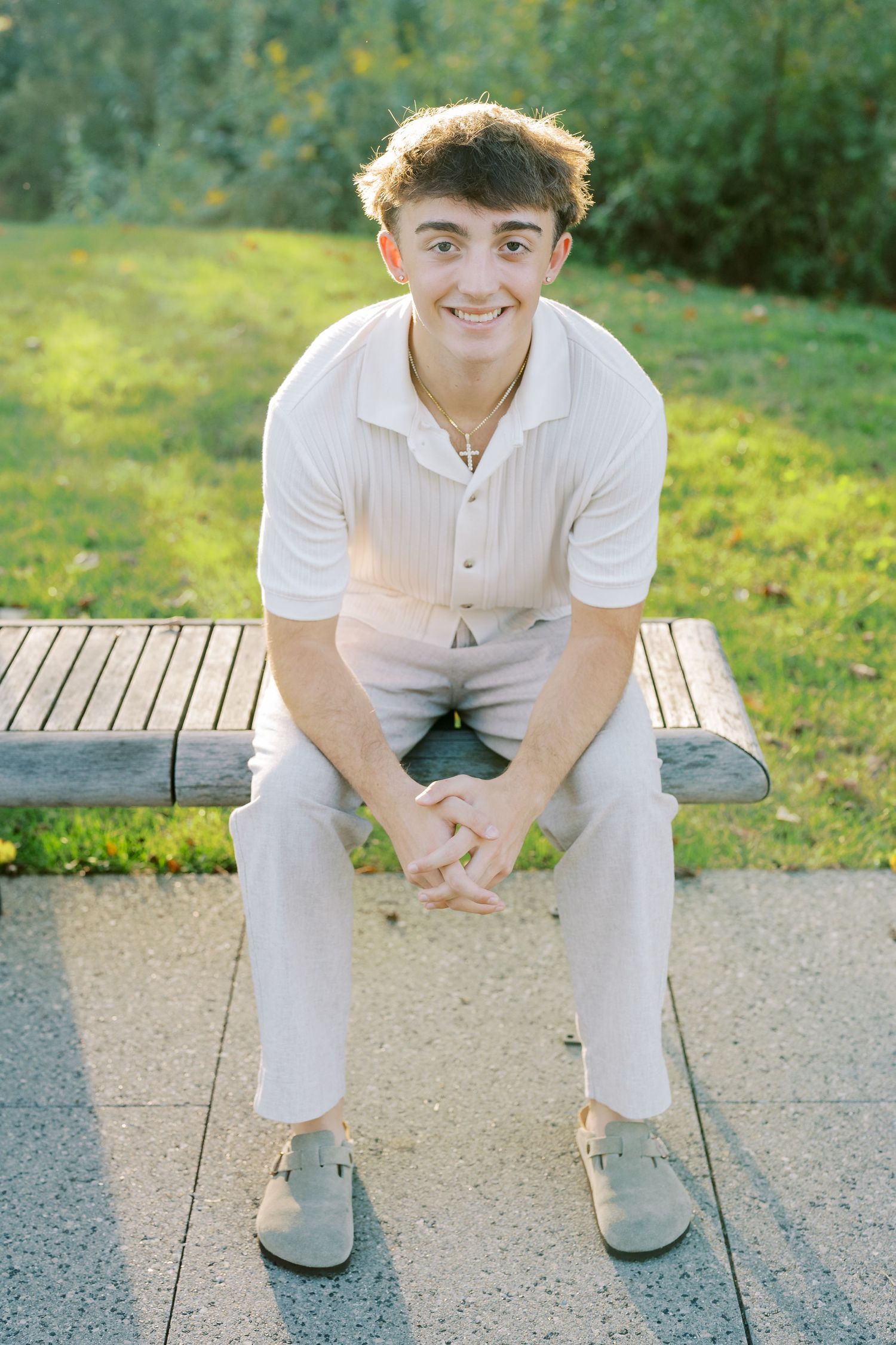 Person in white clothing sits on a wooden deck outdoors in natural sunlit setting.