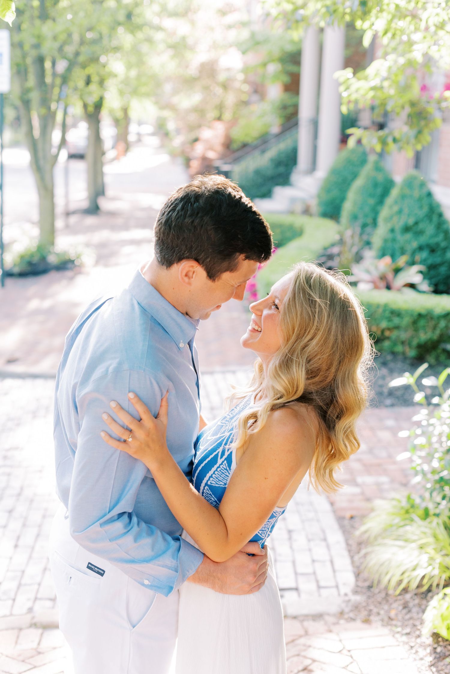 A couple in light blue and white clothing share romantic moments in a sunlit garden path.