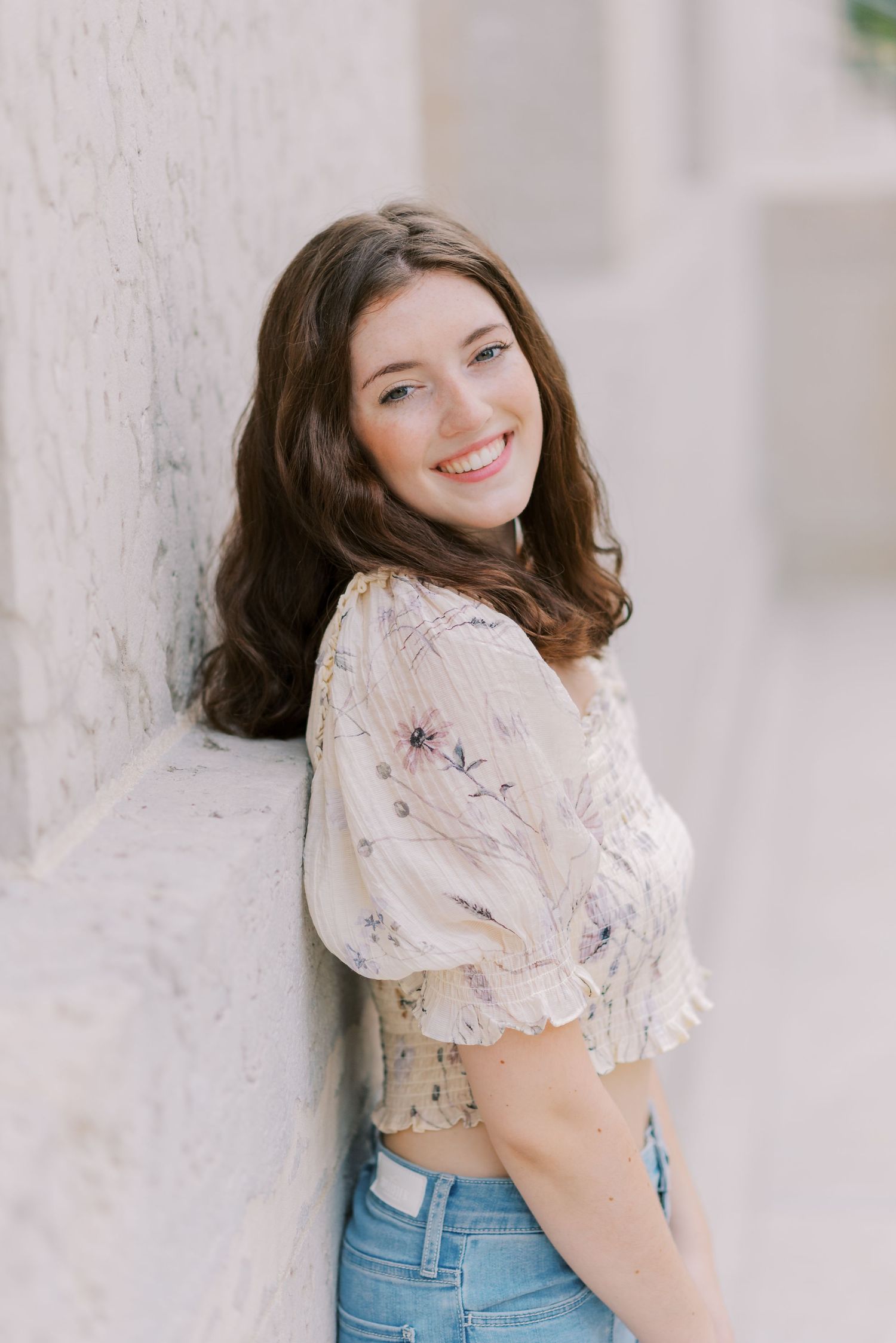 Person in white lace top poses against white wall with natural lighting.