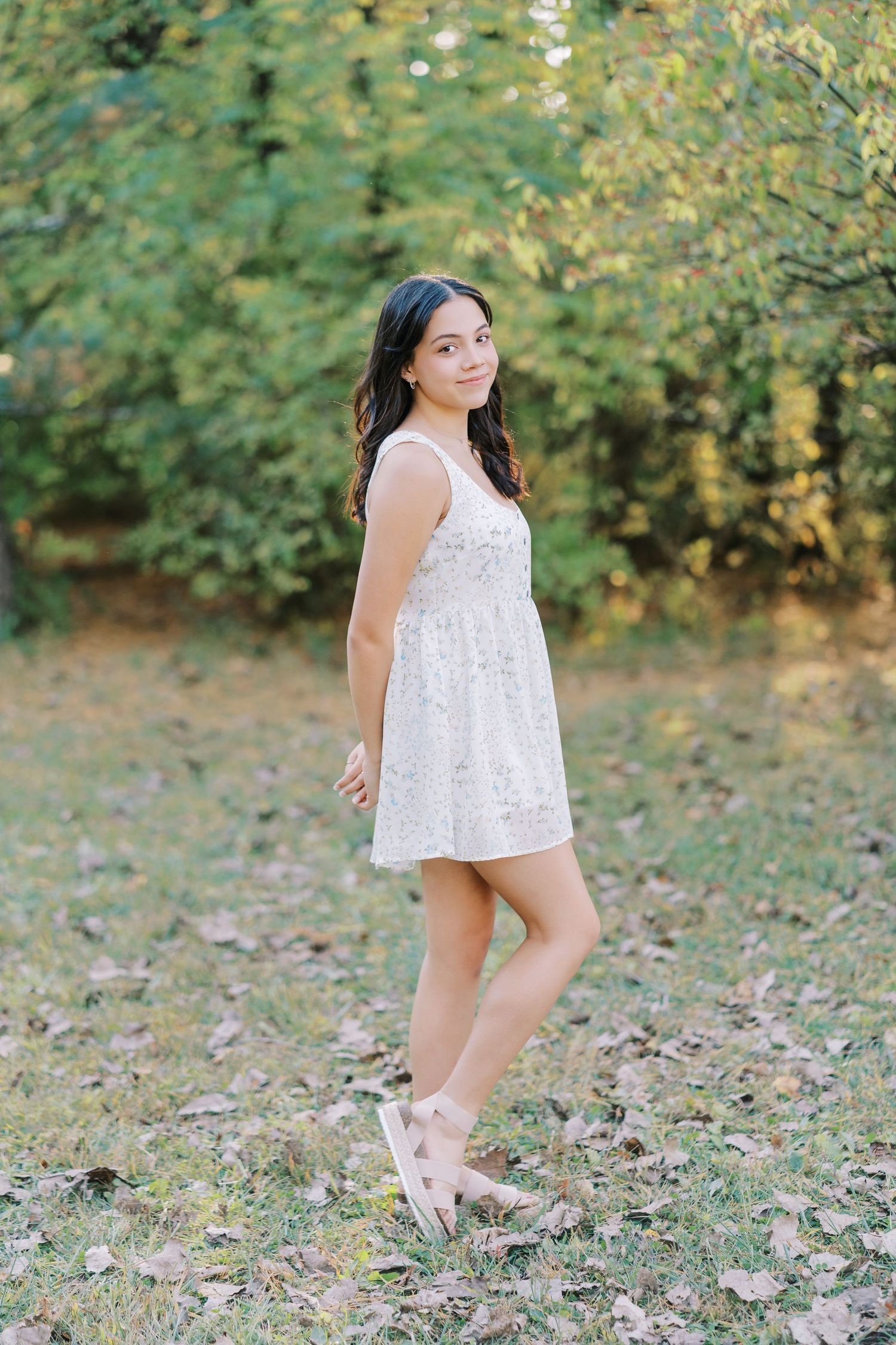 A young girl in a white lace dress dances and twirls playfully in a natural outdoor setting with green foliage.