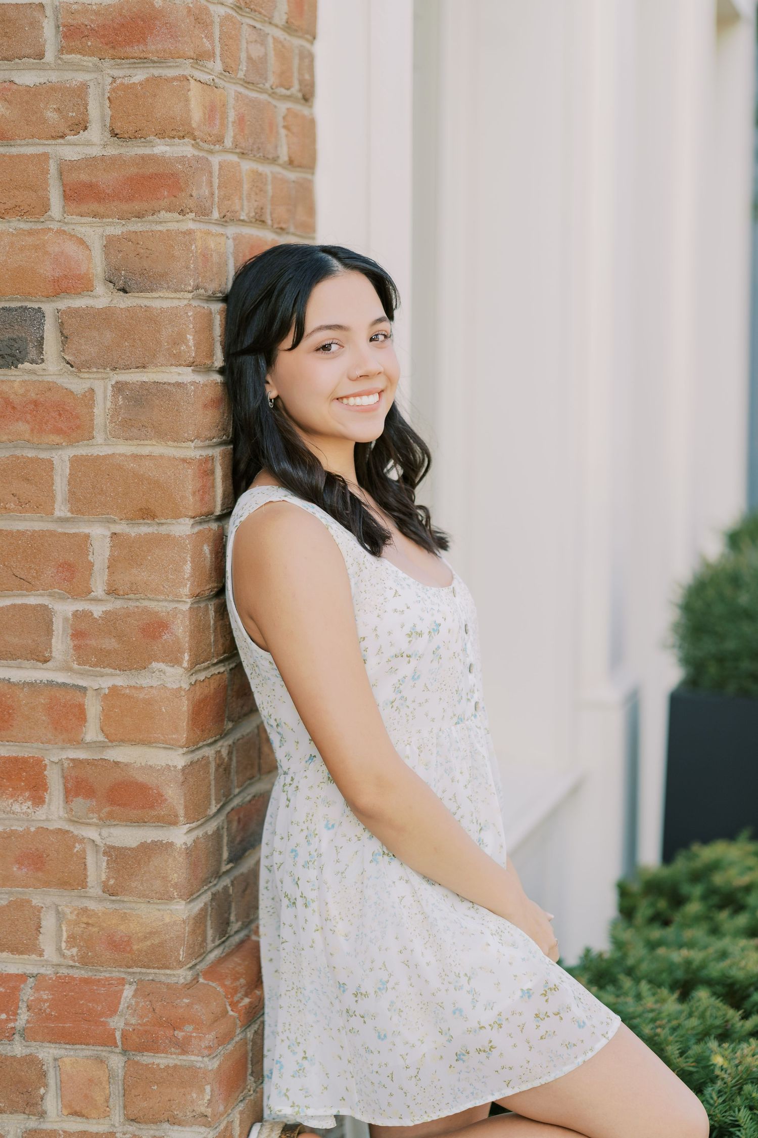 A person in a white lace dress poses against a rustic brick wall in a casual outdoor portrait session.