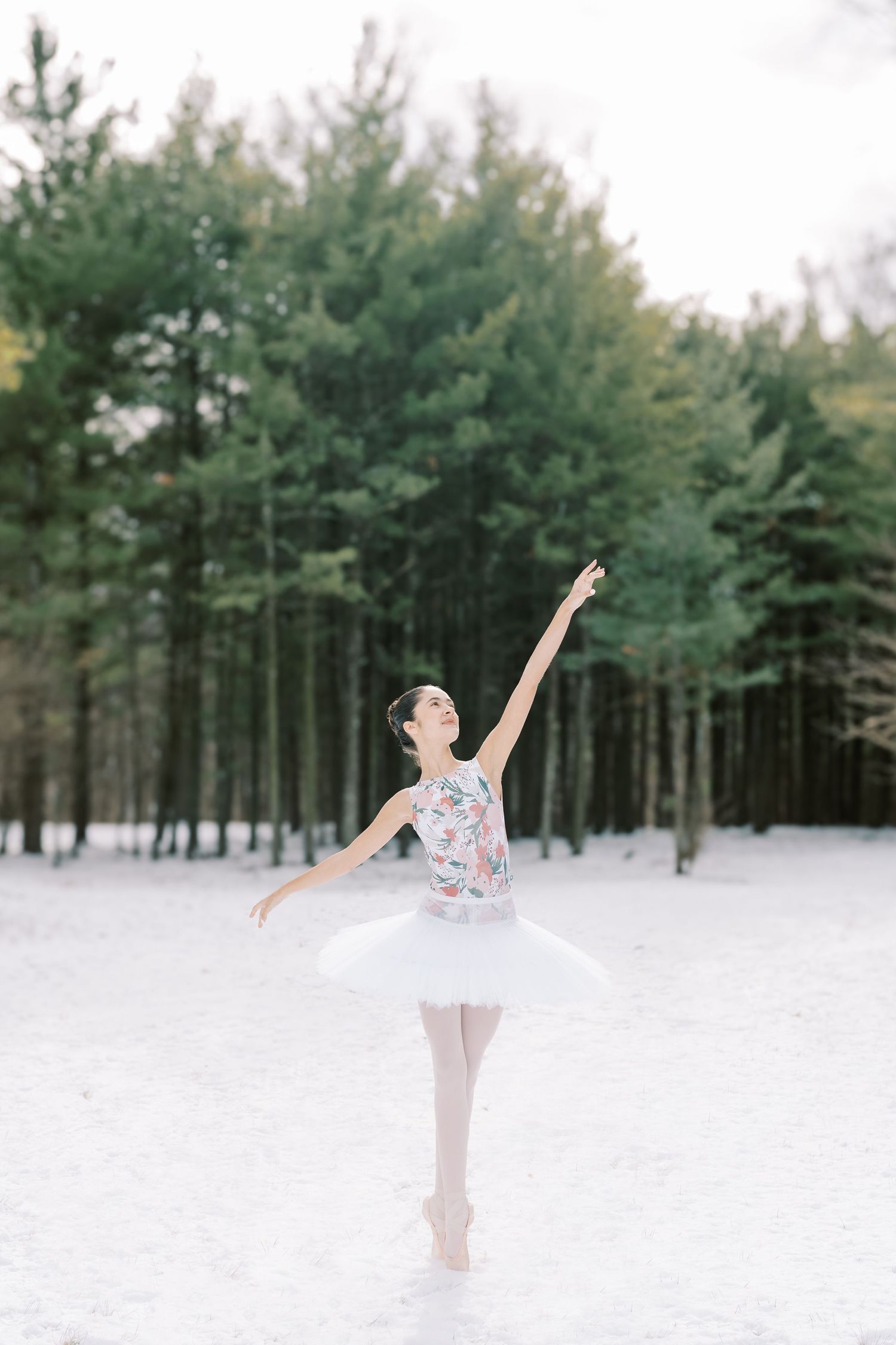 A ballet dancer performs graceful poses in a snowy winter forest landscape with evergreen trees in the background.