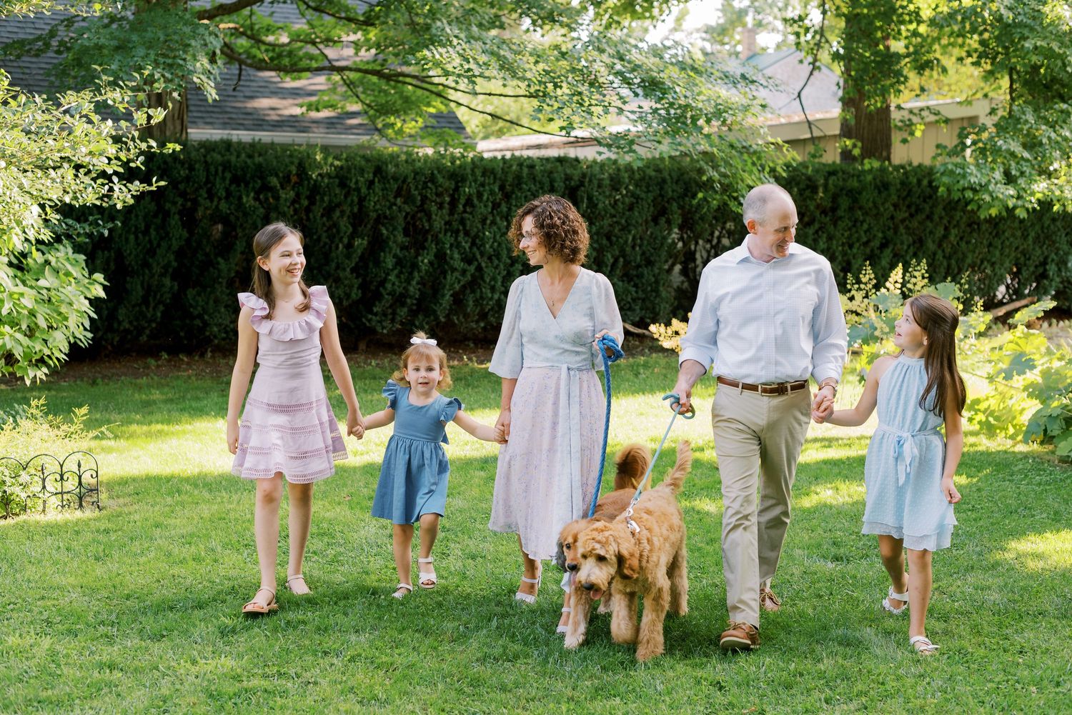 A group portrait session outdoors with family members and dogs arranged on a sunny lawn.