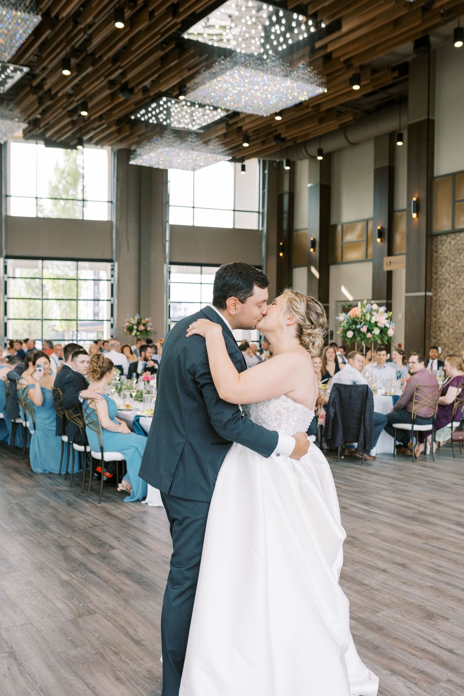 Newlyweds share their first dance in an elegant reception hall with crystal chandeliers and wood floors.