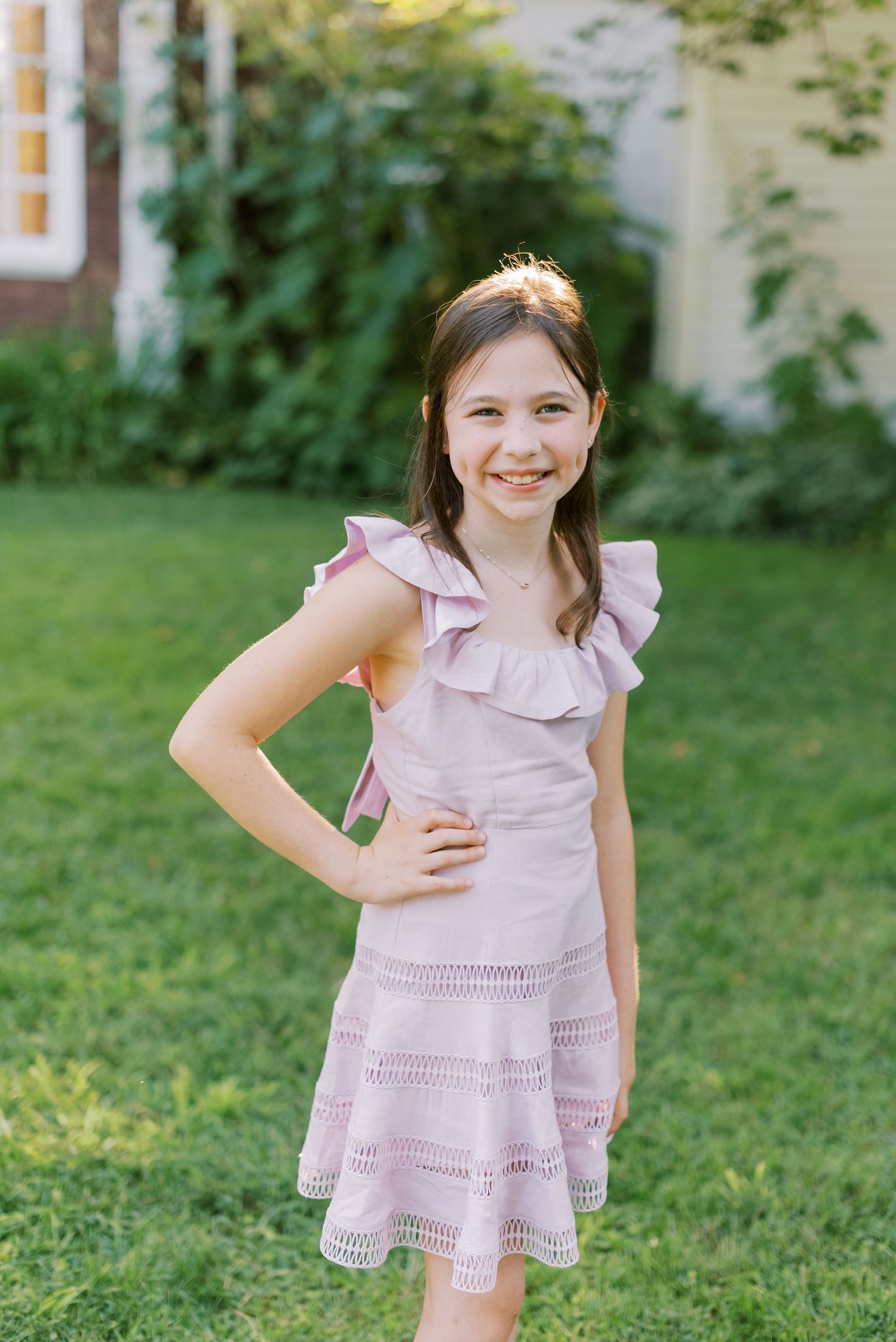 Child in pink ruffled dress posing playfully on grass.