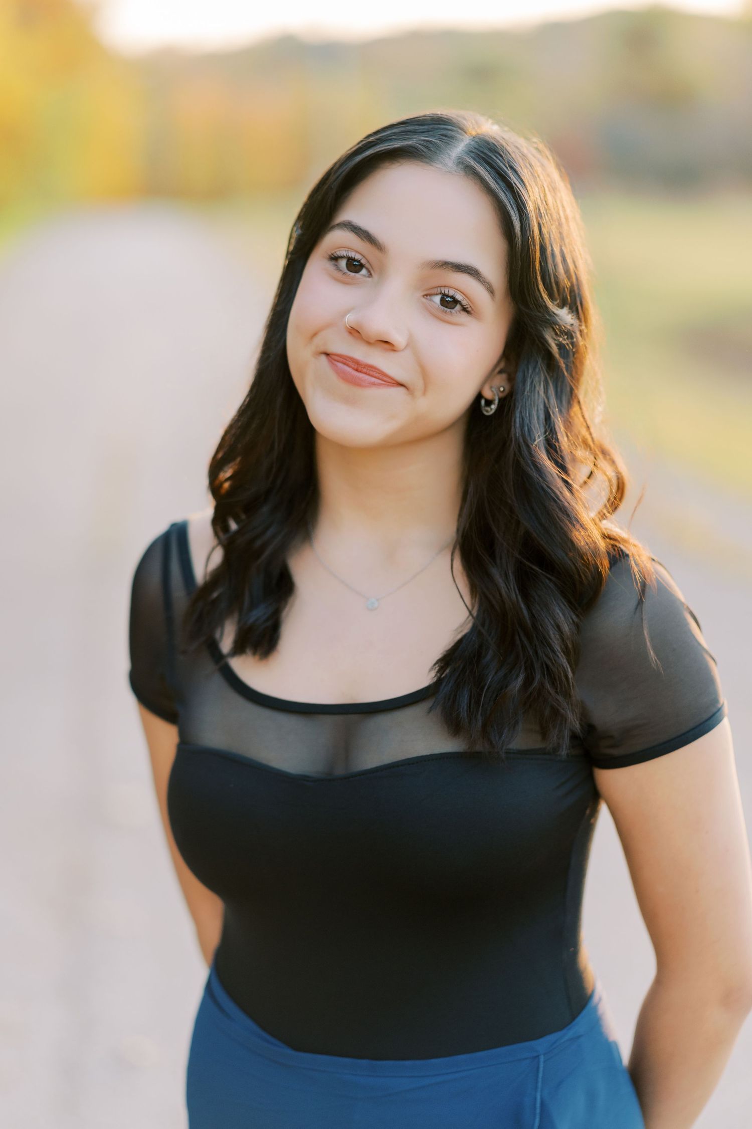 A person wearing a black top poses outdoors in warm lighting with a gentle smile.