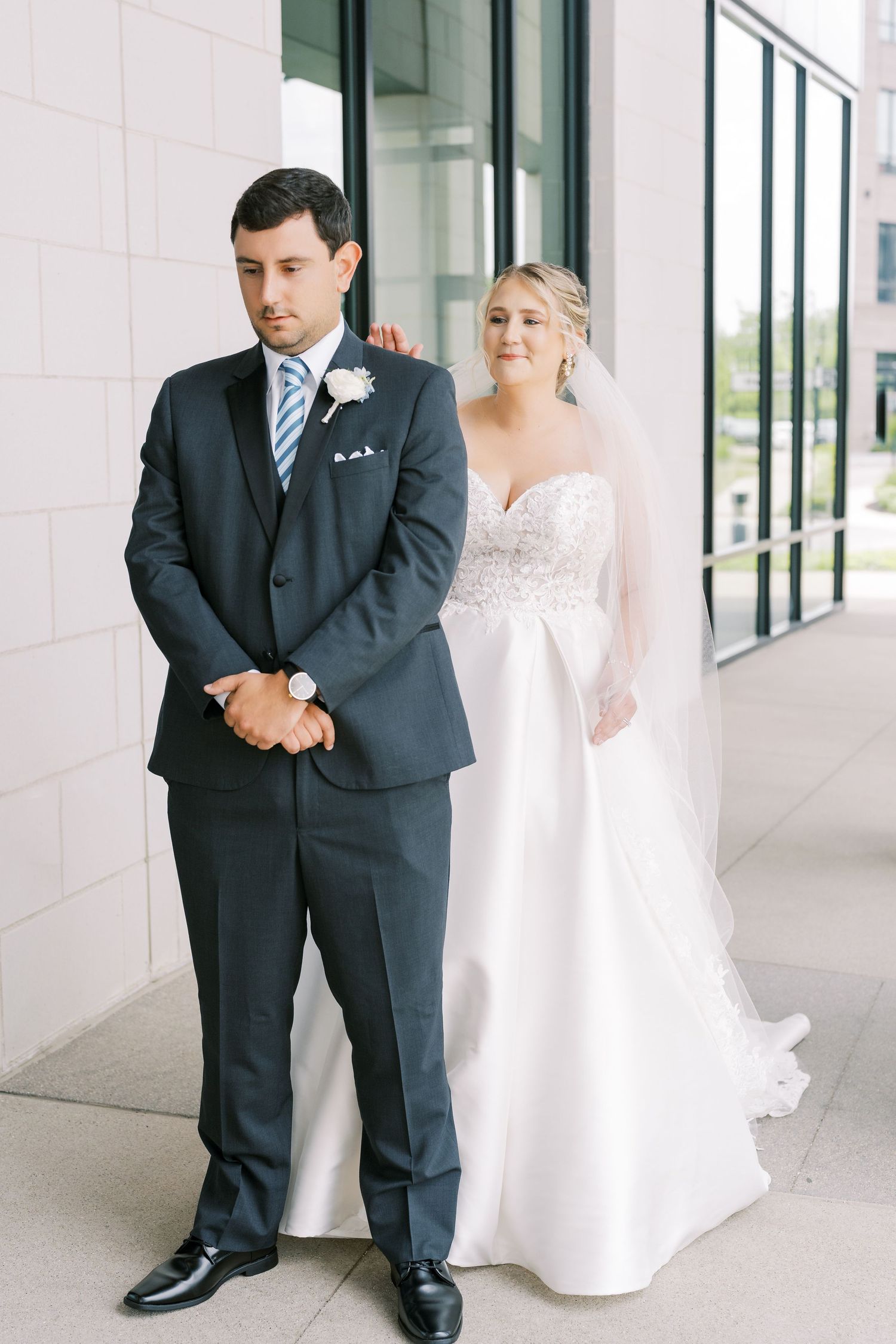 Wedding couple poses elegantly in a modern white hallway with glass windows and columns.