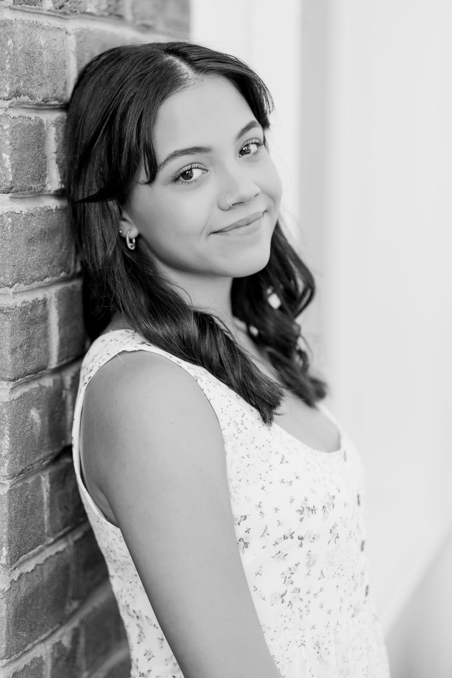 A series of black and white portraits showing a person in a sleeveless white lace dress posing against a brick wall.