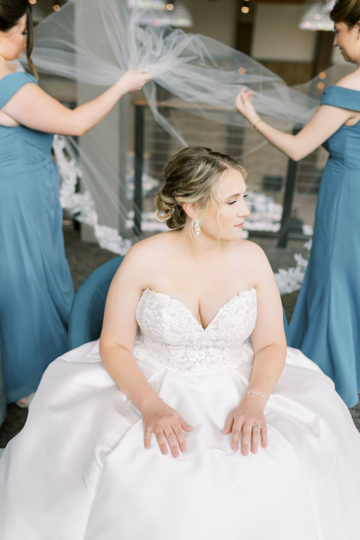 A bride in a white strapless wedding gown poses with bridesmaids wearing dusty blue dresses in a candid moment.