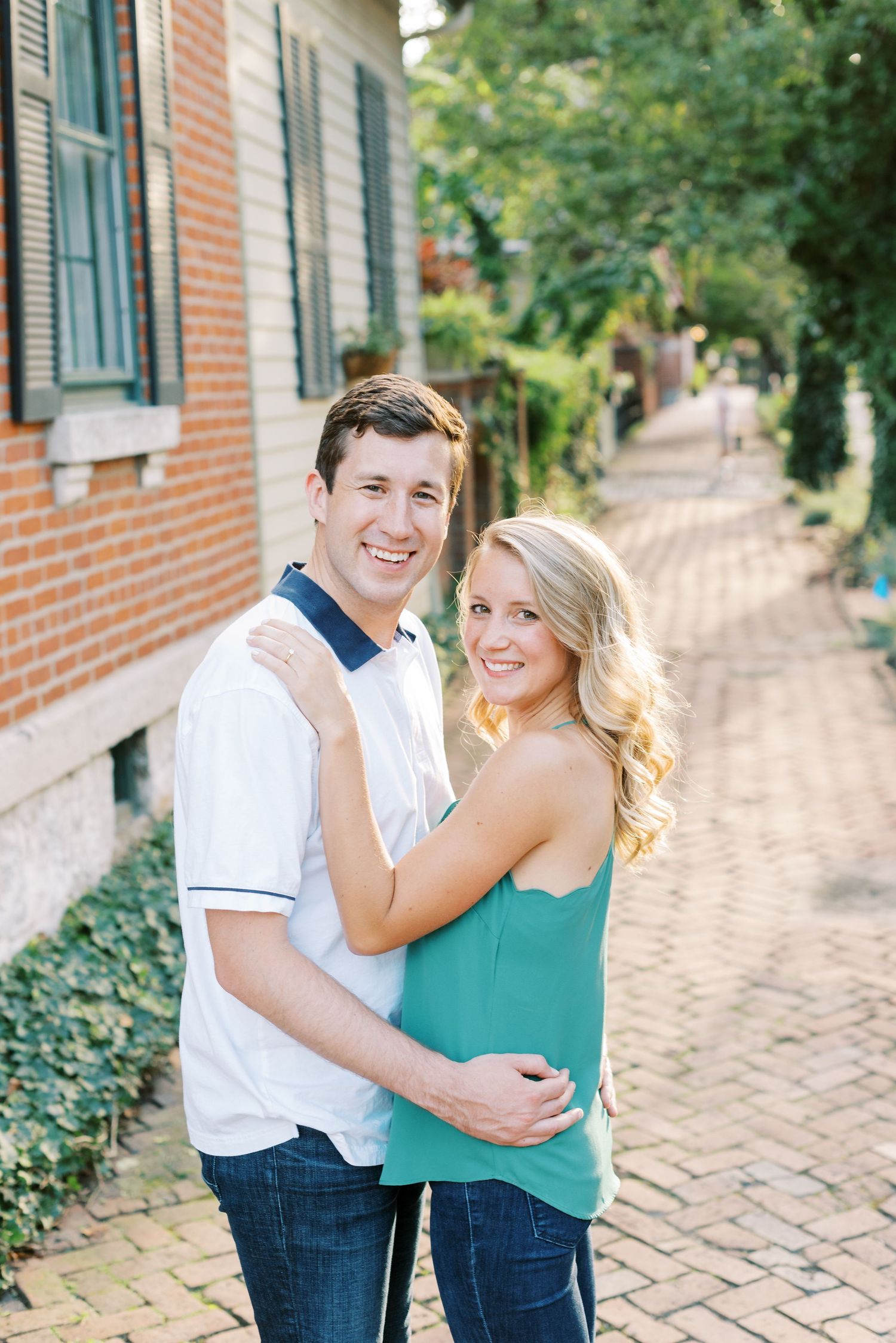 A couple shares joyful moments together on a brick pathway with green foliage in the background.