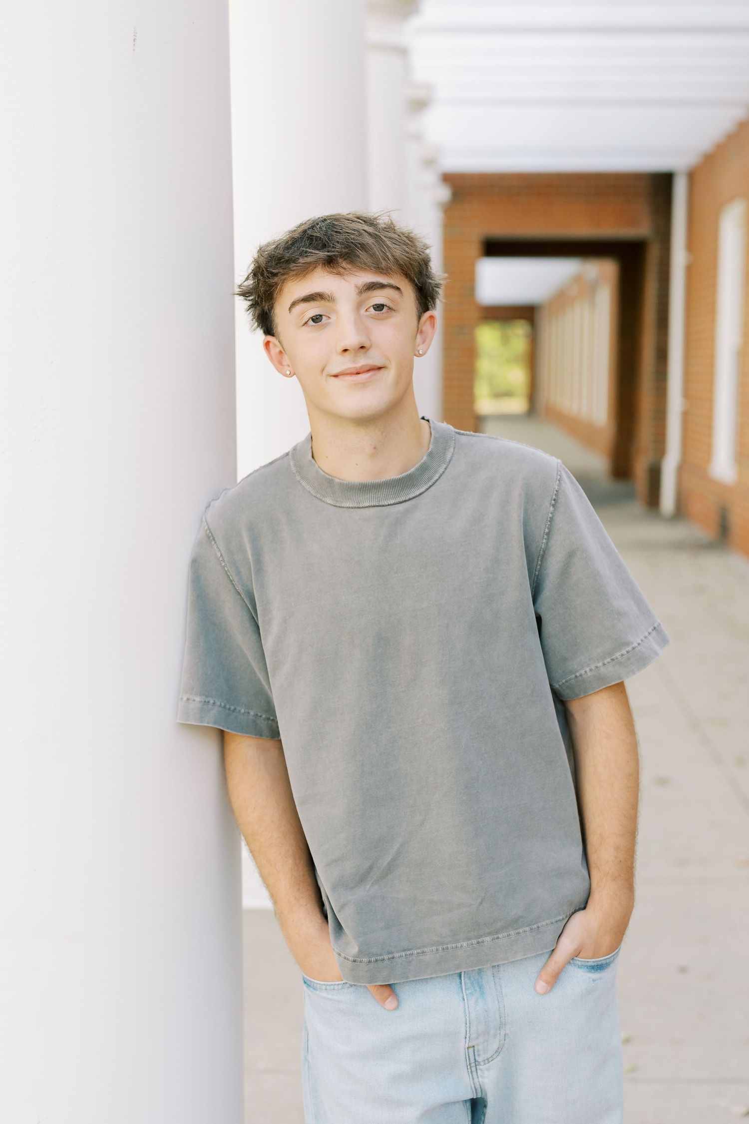 Someone wearing a casual grey cropped t-shirt and light wash jeans poses against a neutral hallway background.