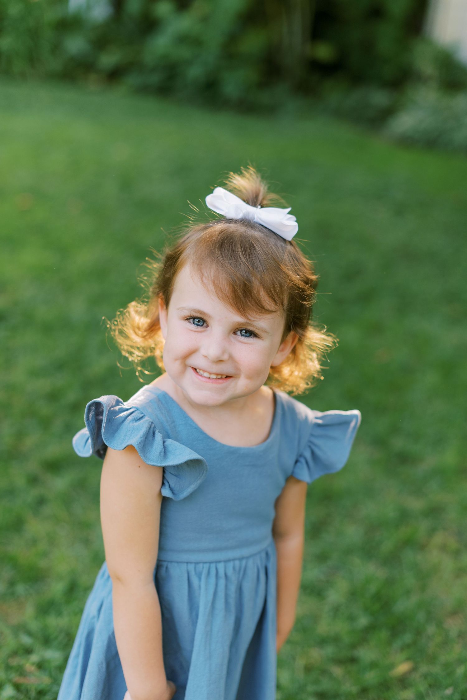 Young child in a blue ruffled dress smiling outdoors in natural lighting.