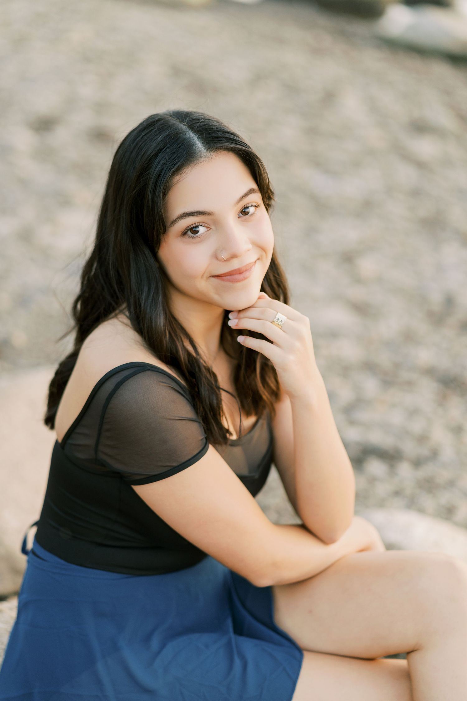 A woman in a black top and blue skirt sits outdoors in a casual portrait series.